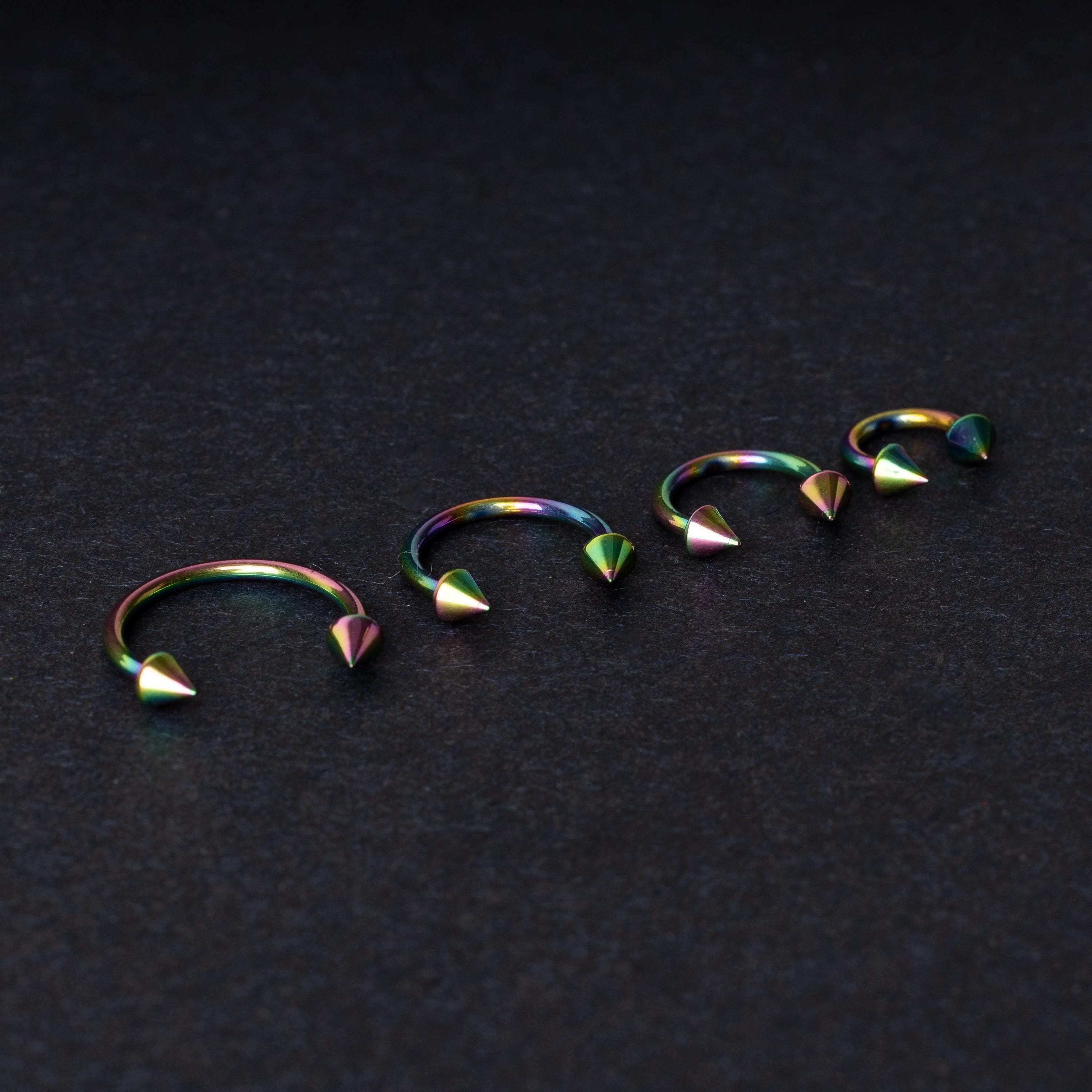 Titanium horseshoe hoops with spike ends, featuring a colorful rainbow finish, displayed on a dark textured background.