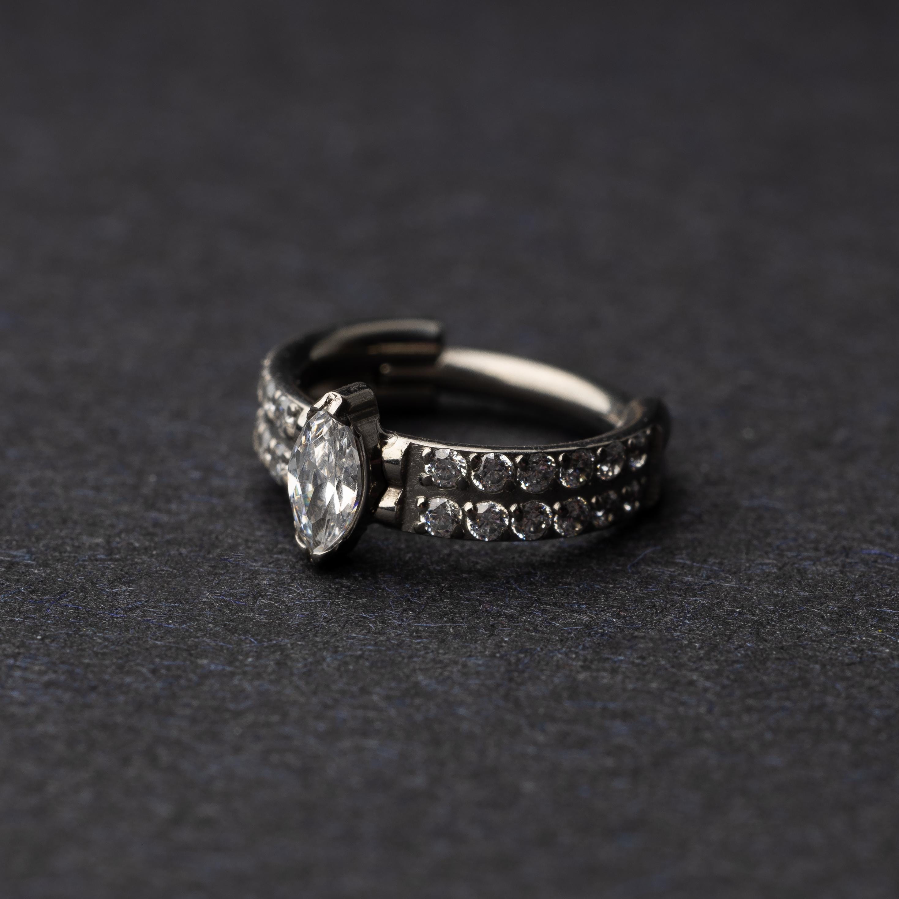 A close-up of a marquise gemstone septum or helix clicker with dual rows of sparkling gems displayed on a dark background.