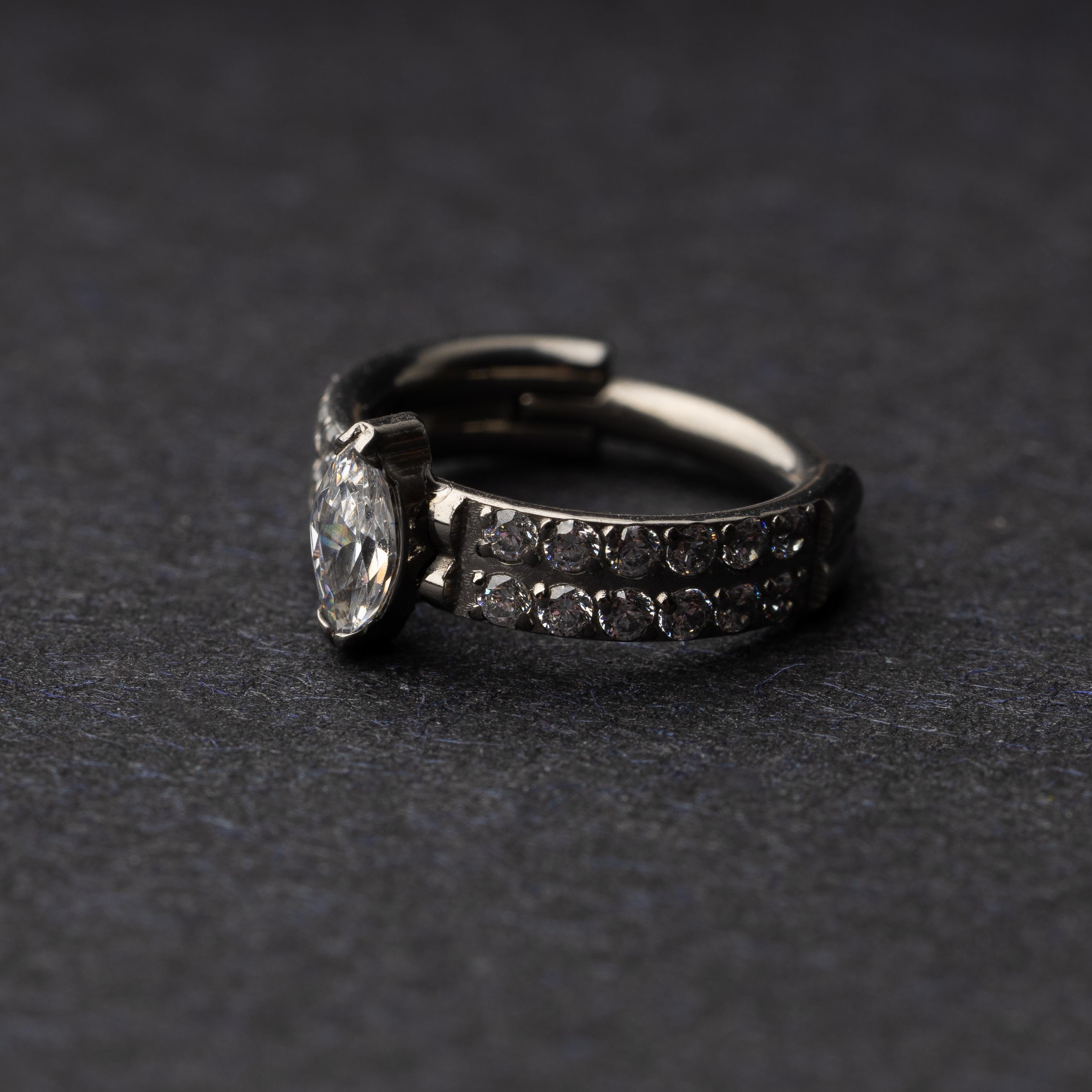 A close-up of a marquise gemstone septum or helix clicker with dual rows of sparkling gems displayed on a dark background.