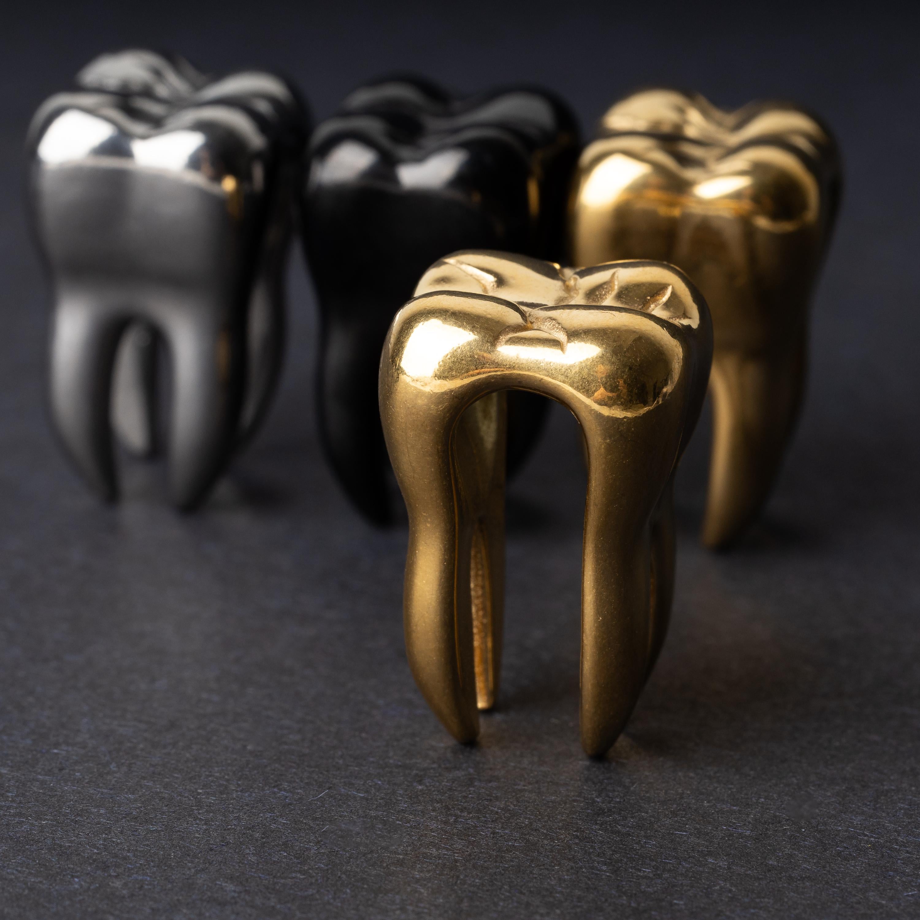Close-up of gold tooth-shaped ear weights with polished detailing, displayed on a dark background.