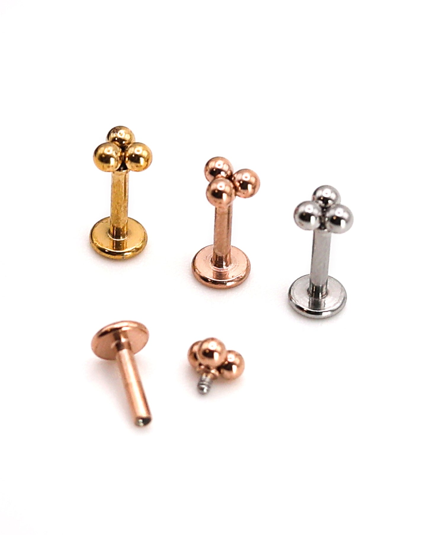Close-up of three minimalist ball cluster labret studs in rose gold, silver, and gold finishes, displayed on a light background.