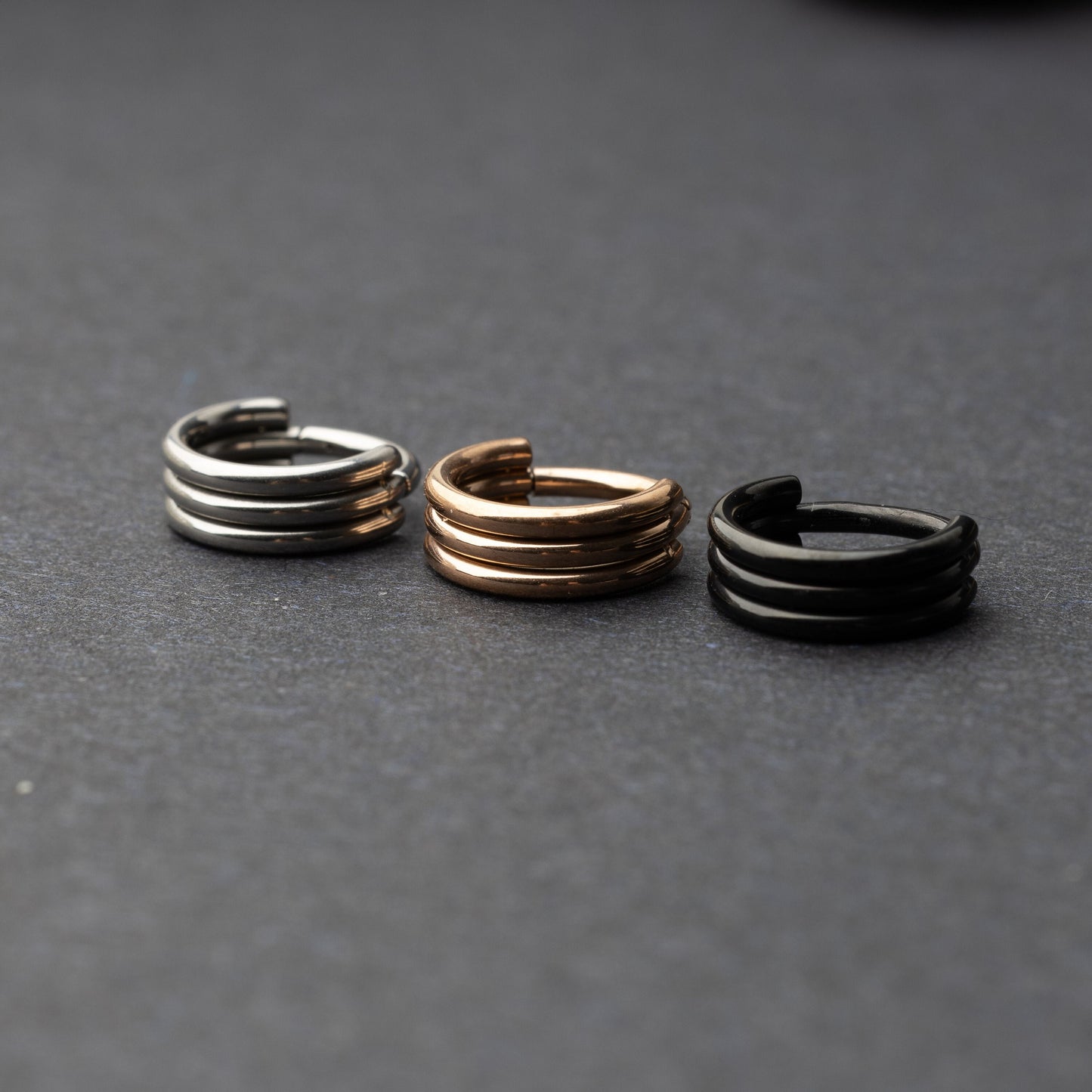 Triple-band seamless hoop rings in silver, gold, and black finishes displayed on a dark background, highlighting their sleek and modern design.