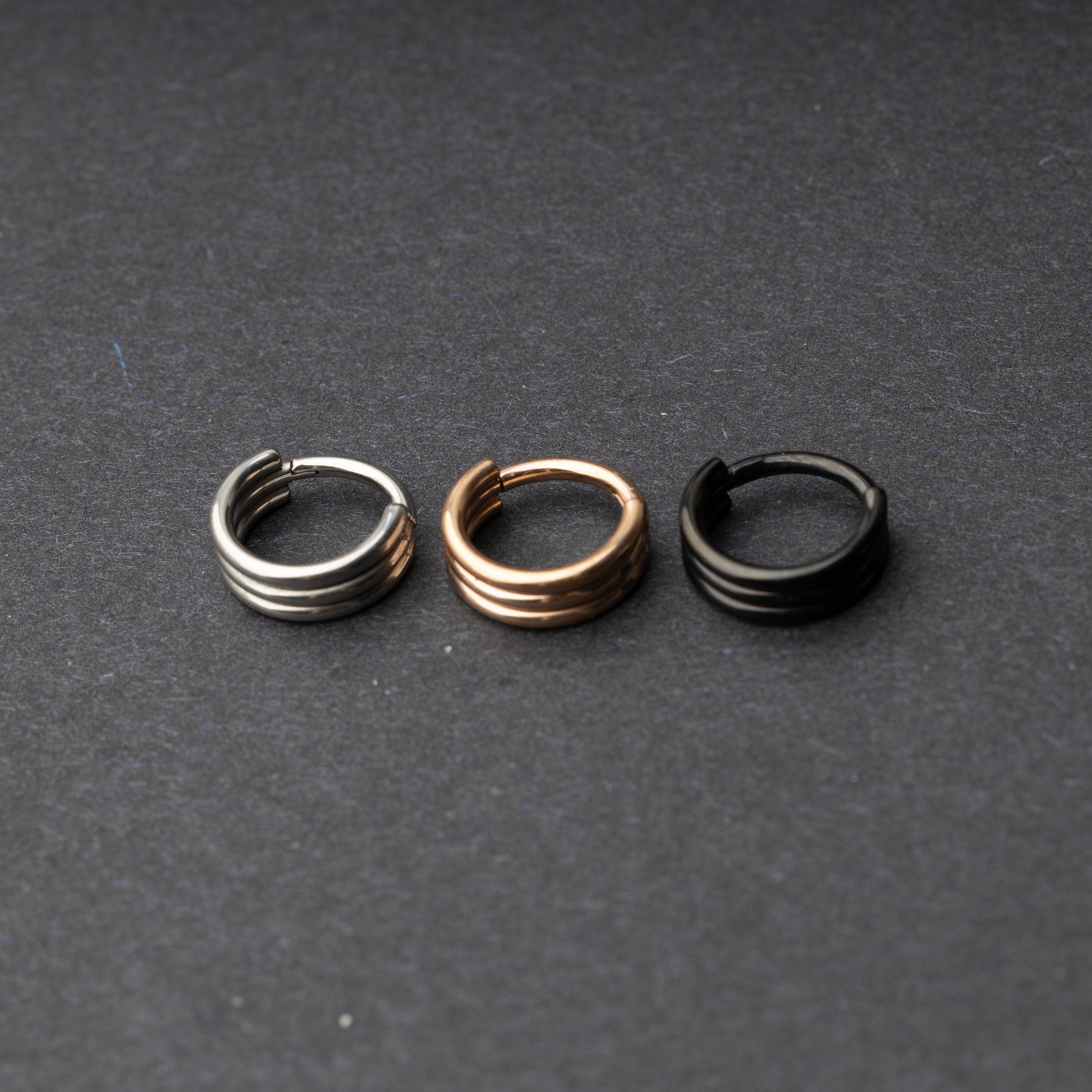 Triple-band seamless hoop rings in silver, gold, and black finishes displayed on a dark background, highlighting their sleek and modern design.