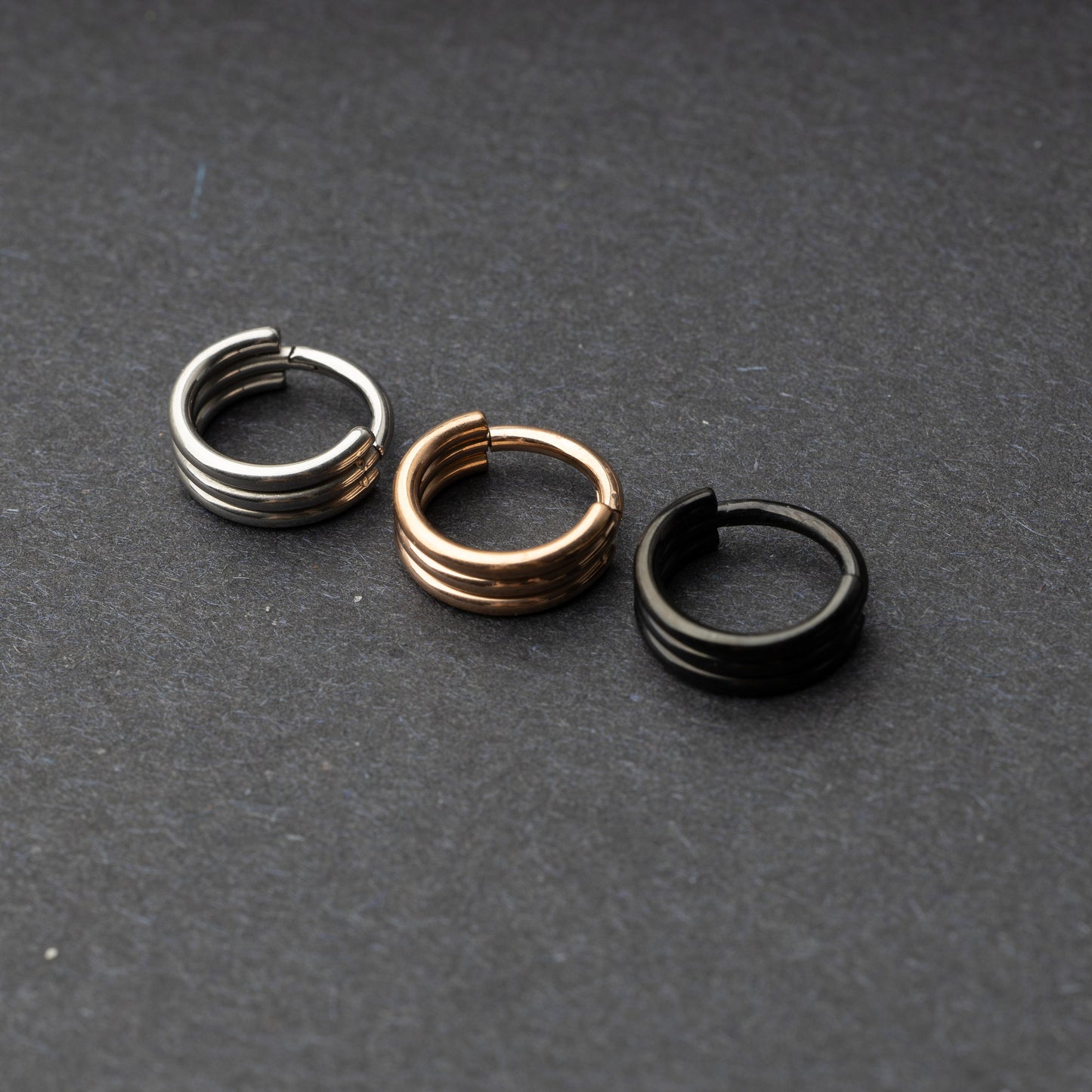 Triple-band seamless hoop rings in silver, gold, and black finishes displayed on a dark background, highlighting their sleek and modern design.