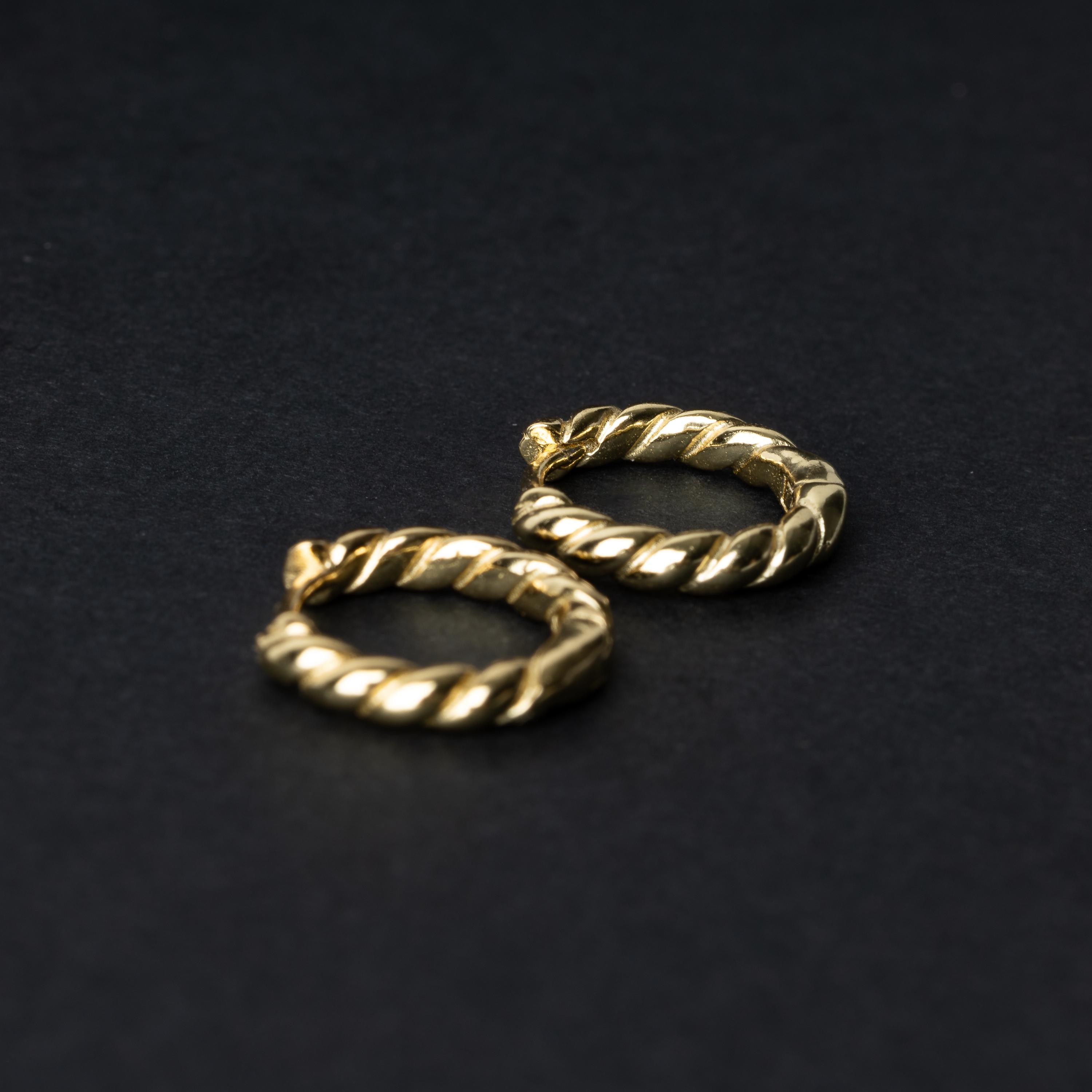Pair of small gold braided hoop earrings, displayed on a dark background.