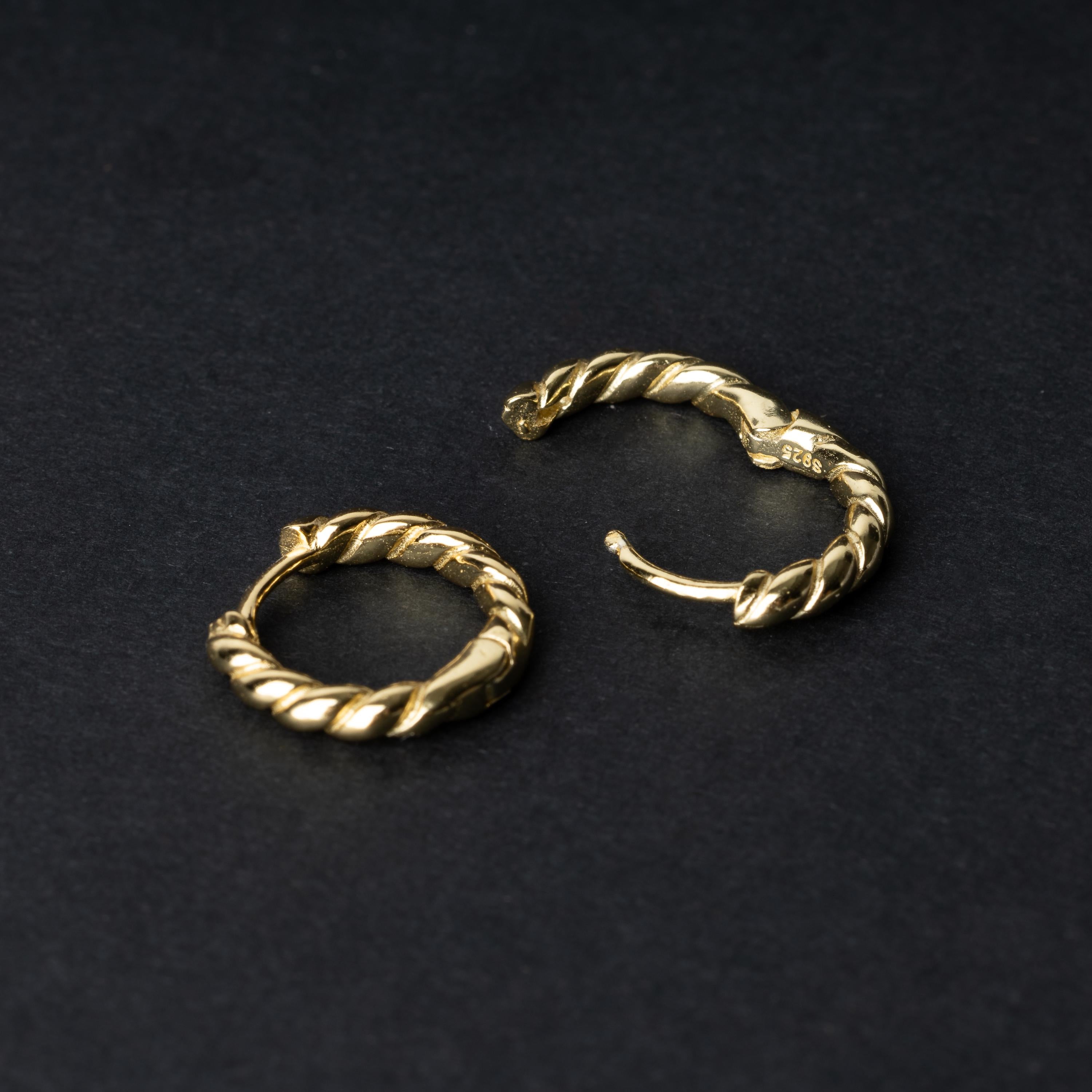 Pair of small gold braided hoop earrings, displayed on a dark background.