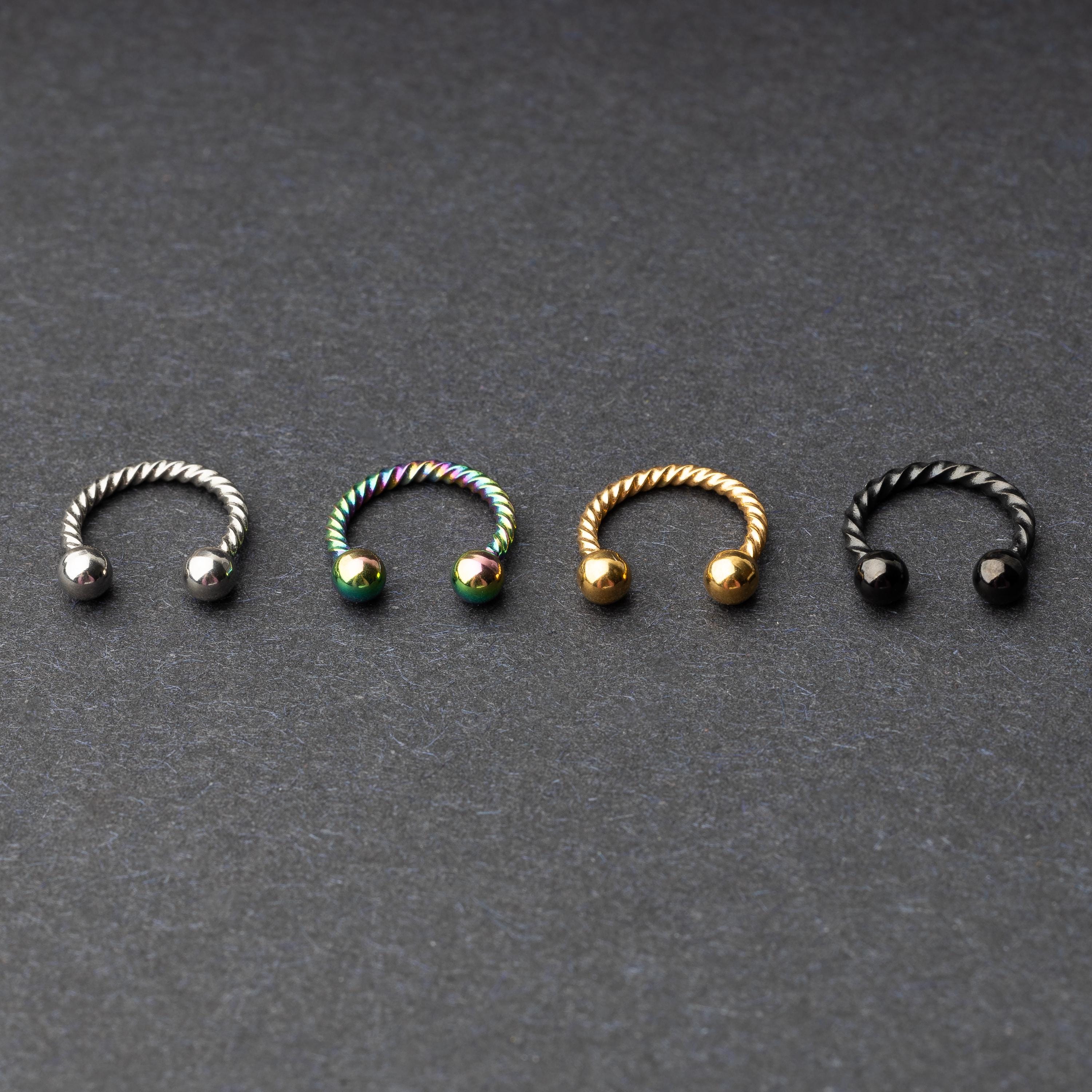 Twisted horseshoe barbells in silver, rainbow, gold, and black finishes displayed on a dark background, highlighting their bold and unique design.