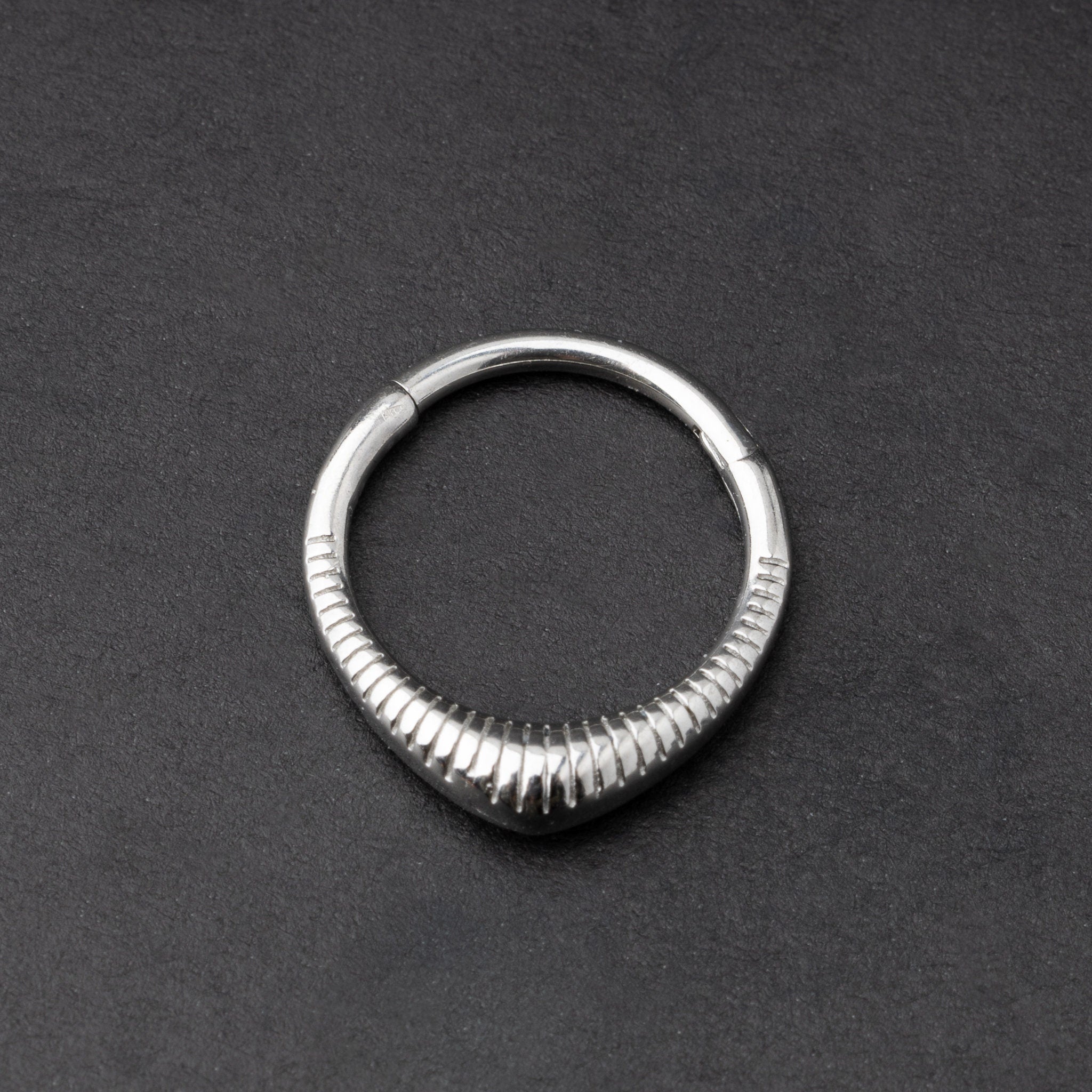 Gold and silver ribbed septum clicker jewelry displayed on a dark background, showcasing a sleek, modern design.