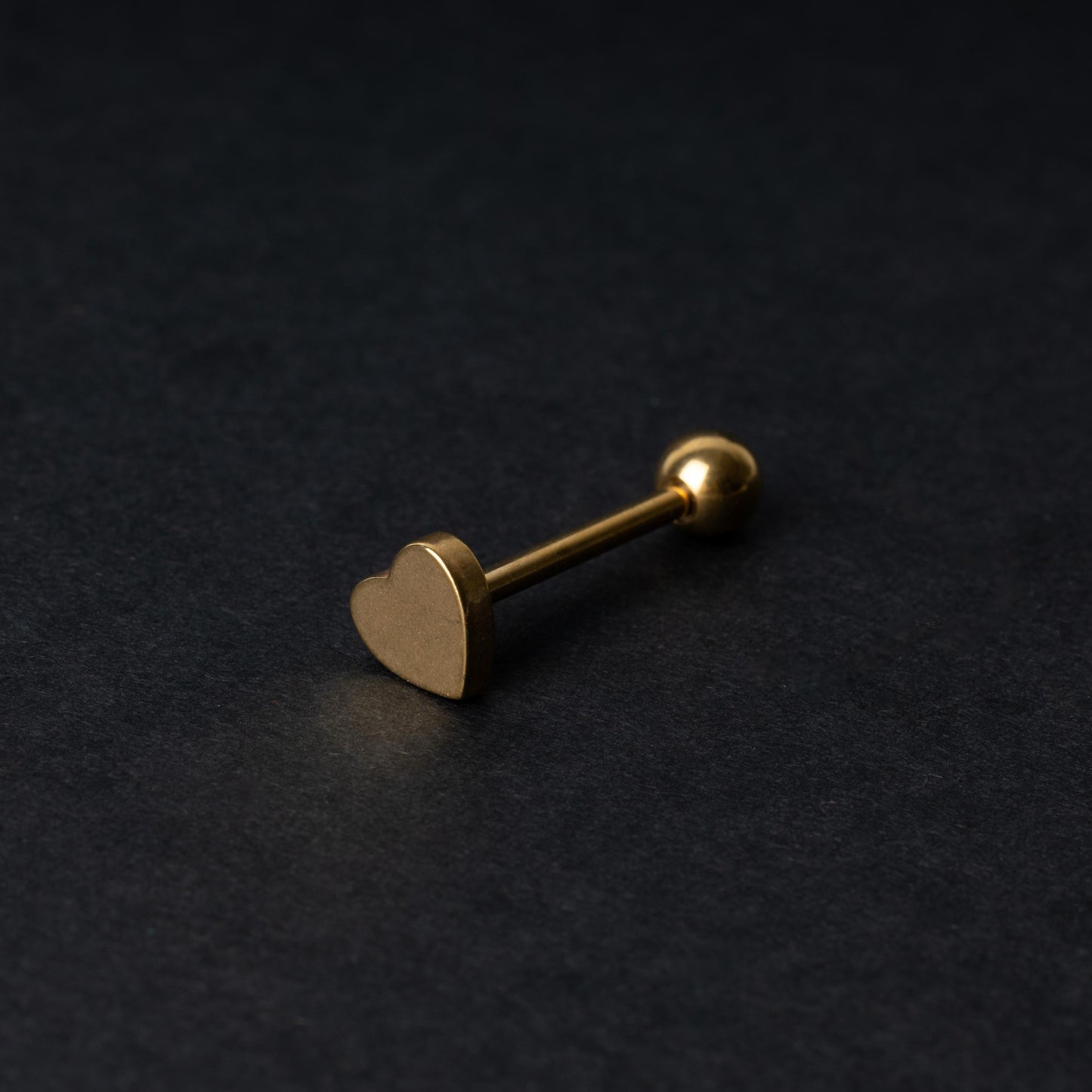 Heart shaped tongue bar in gold, displayed on a dark background.