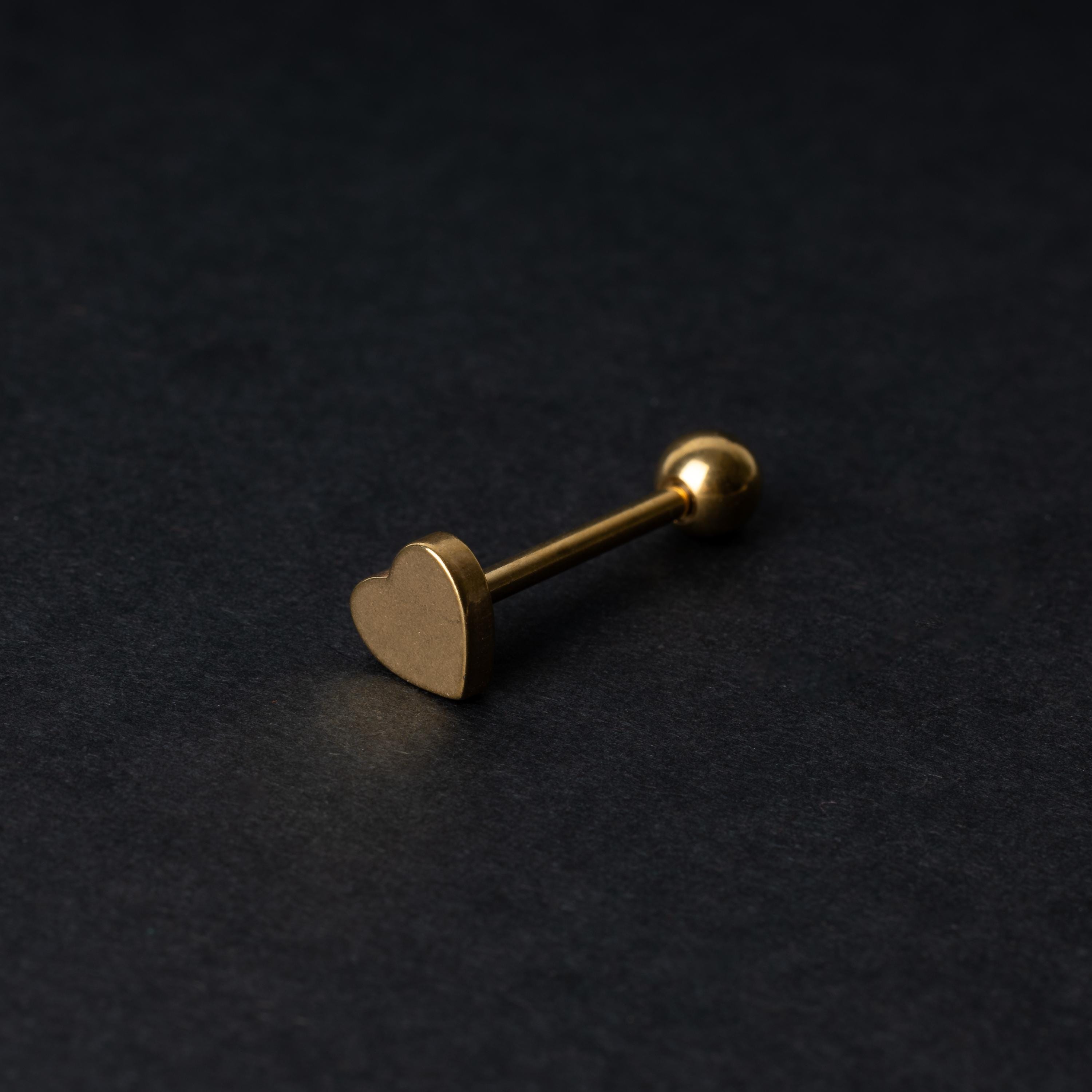 Heart shaped tongue bar in gold, displayed on a dark background.