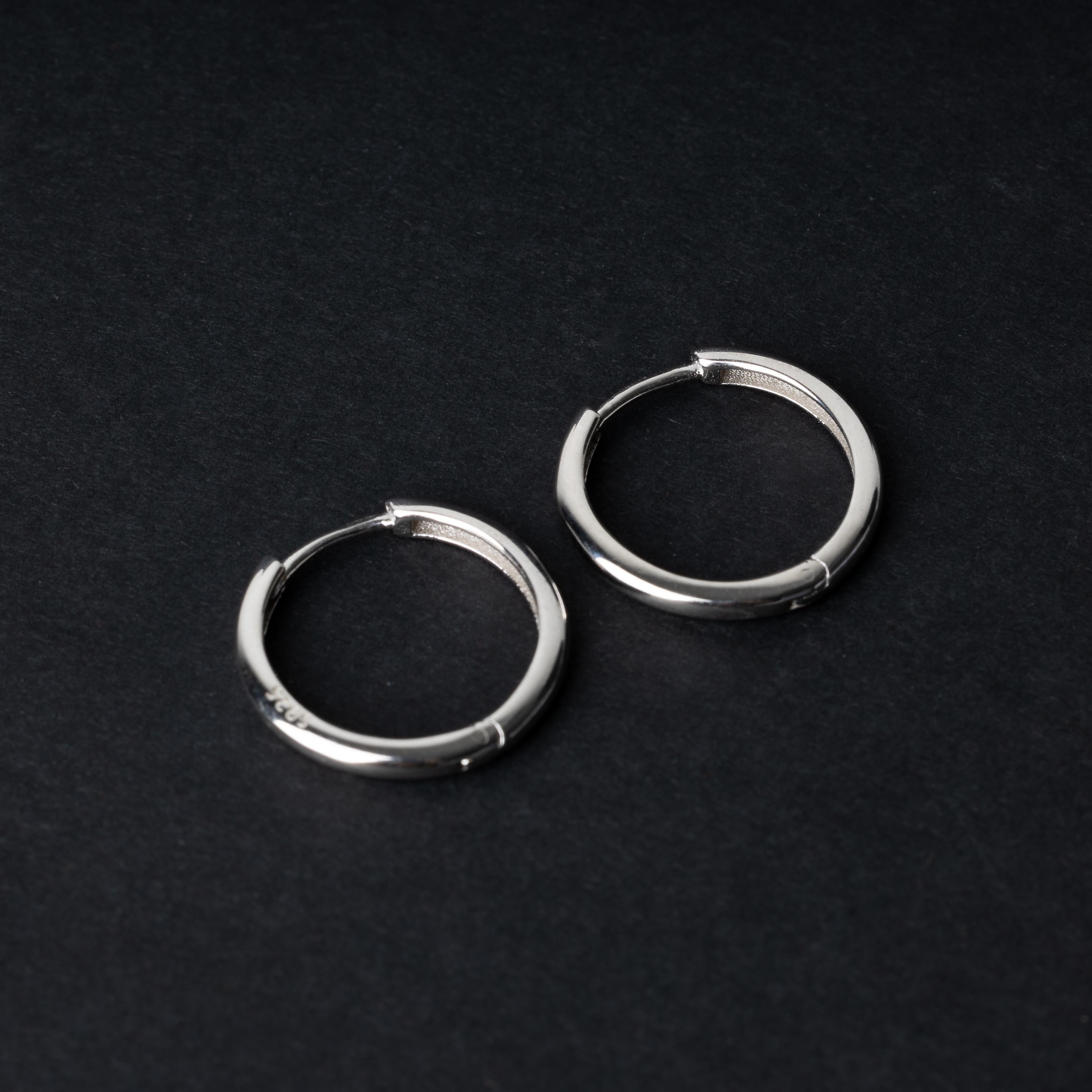A pair of hoop earrings in silver displayed on a dark background