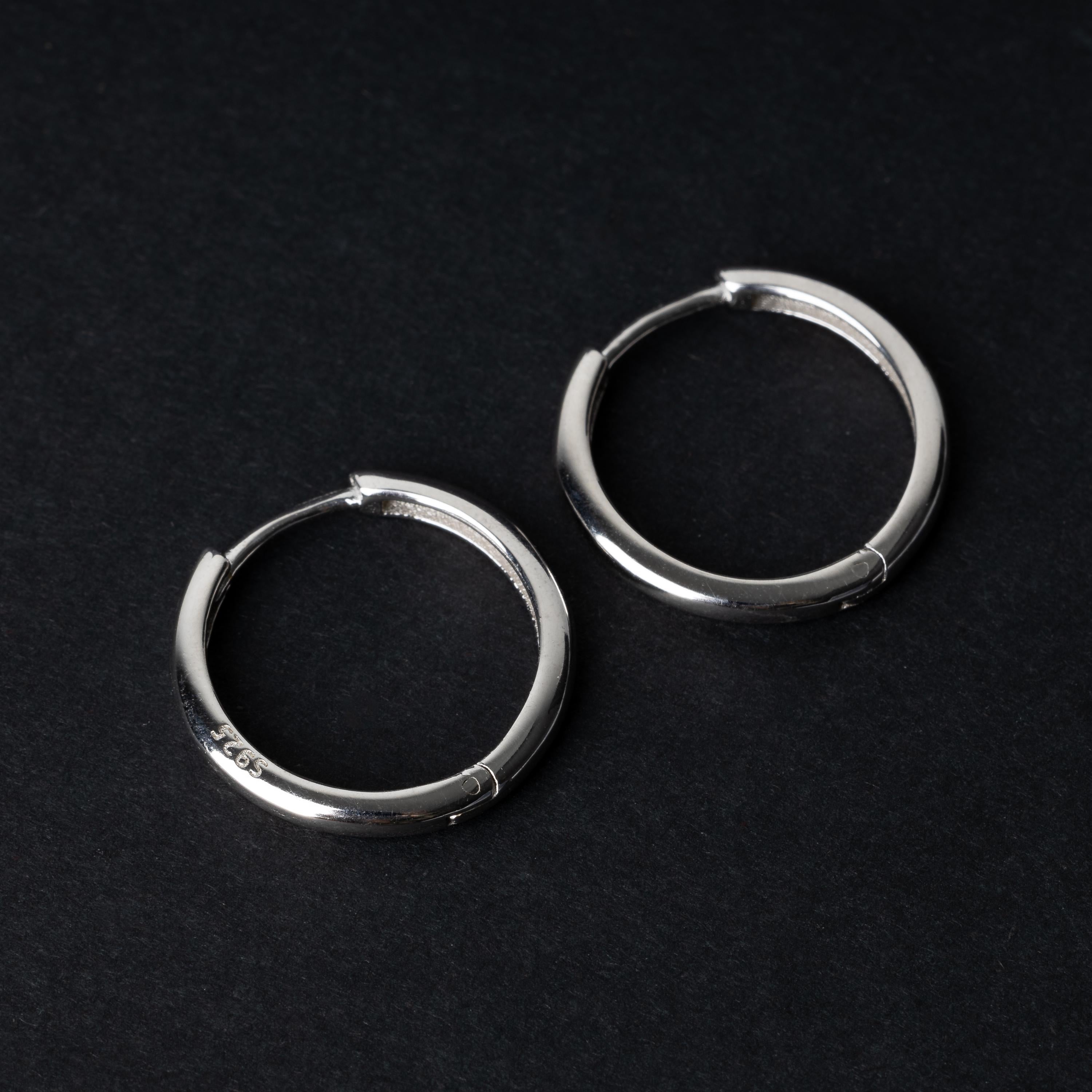 A pair of hoop earrings in silver displayed on a dark background