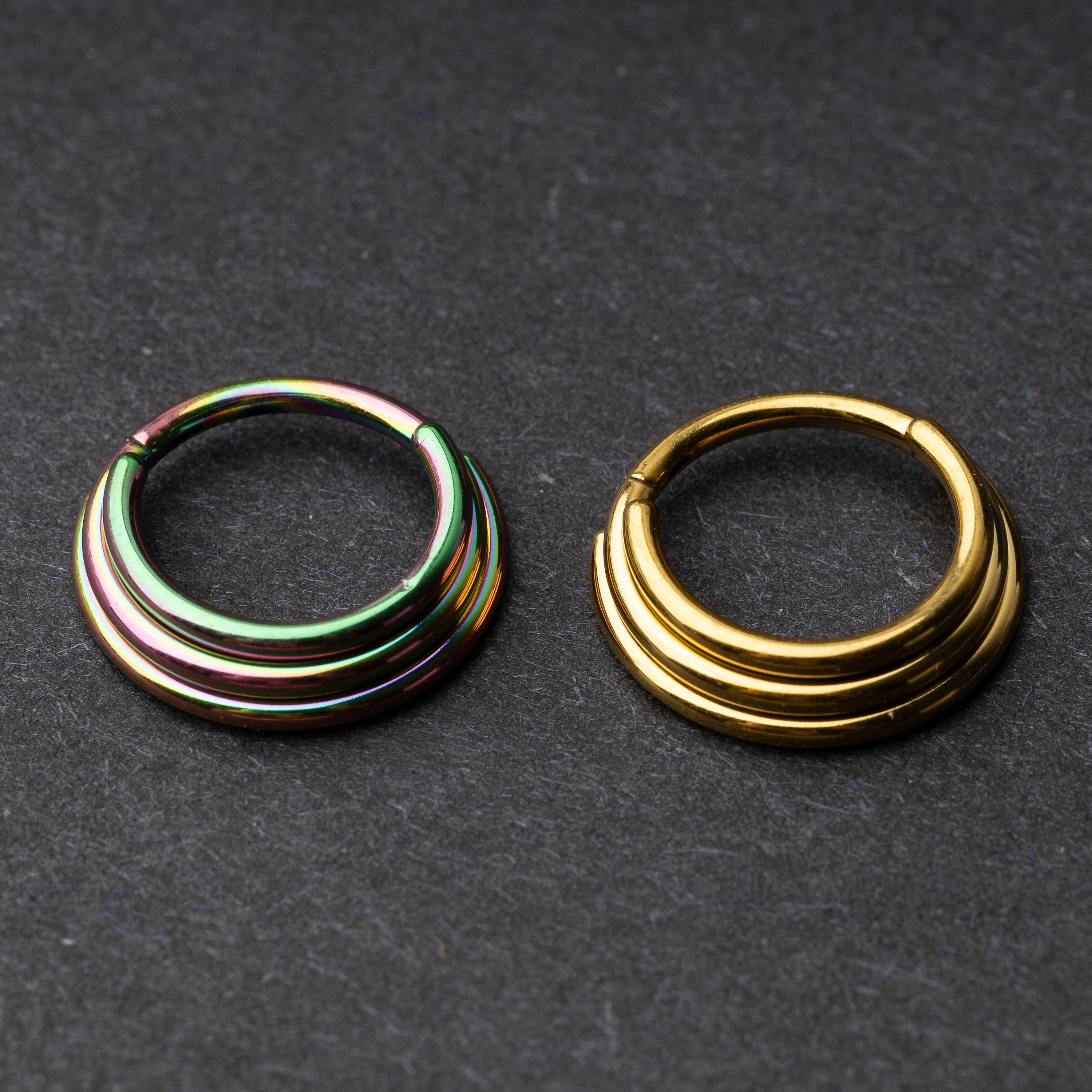 Rainbow and gold-colored layered stacked clicker rings displayed on a dark background.