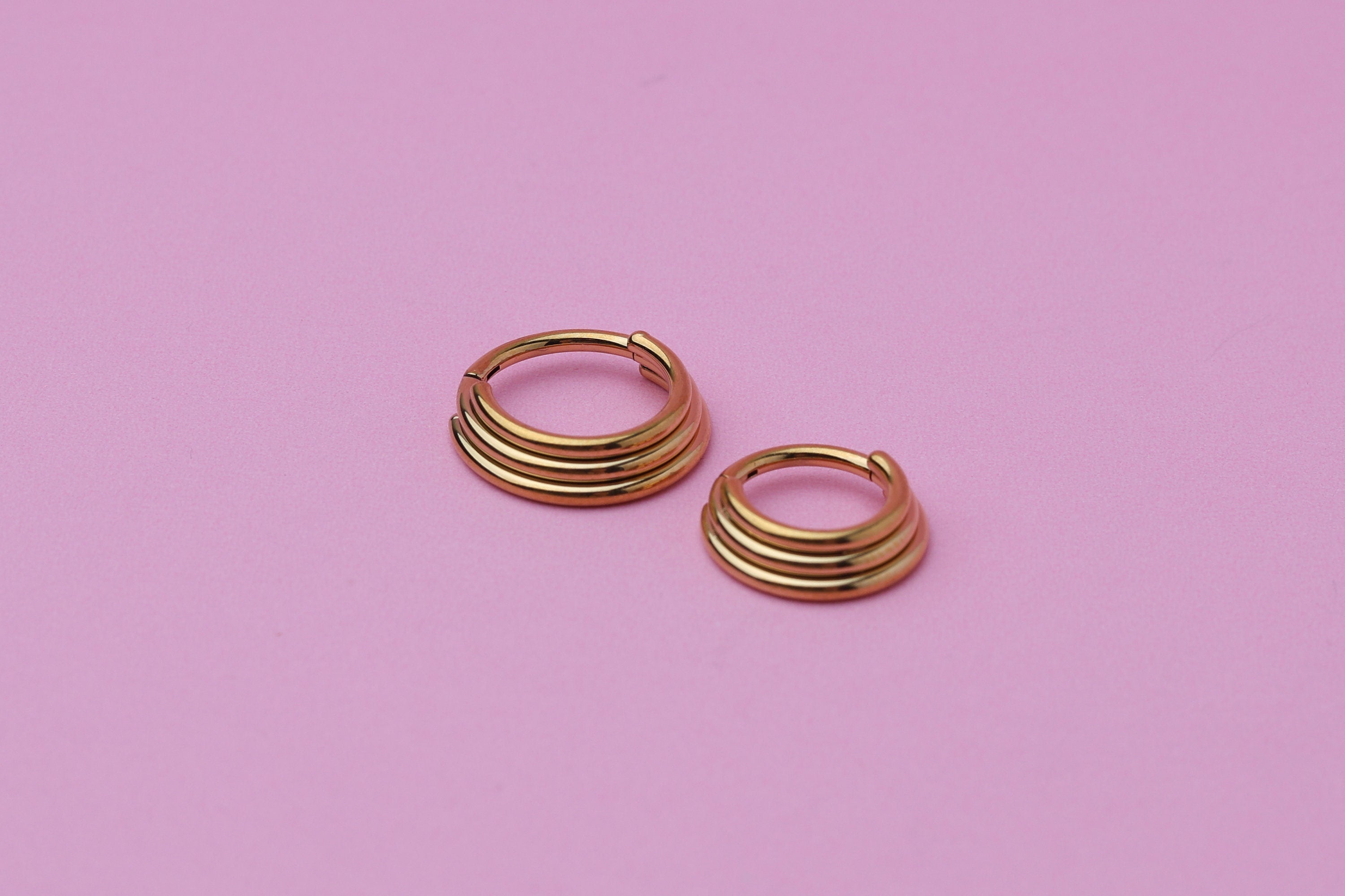 Stacked Septum Clicker in gold on a pink background.