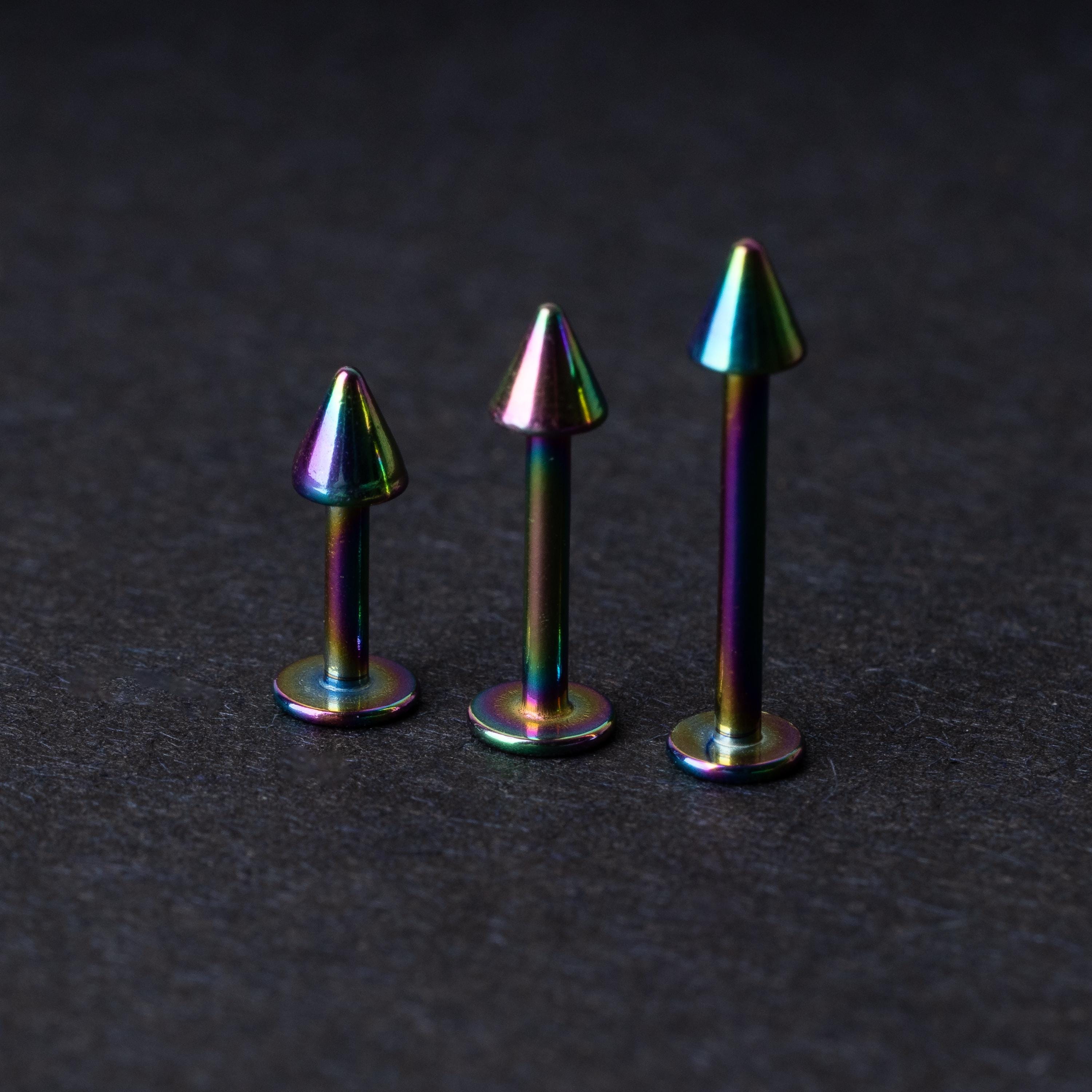 Three rainbow labret studs with cone-shaped tops displayed on a dark background, highlighting their iridescent finish and sleek, durable design.