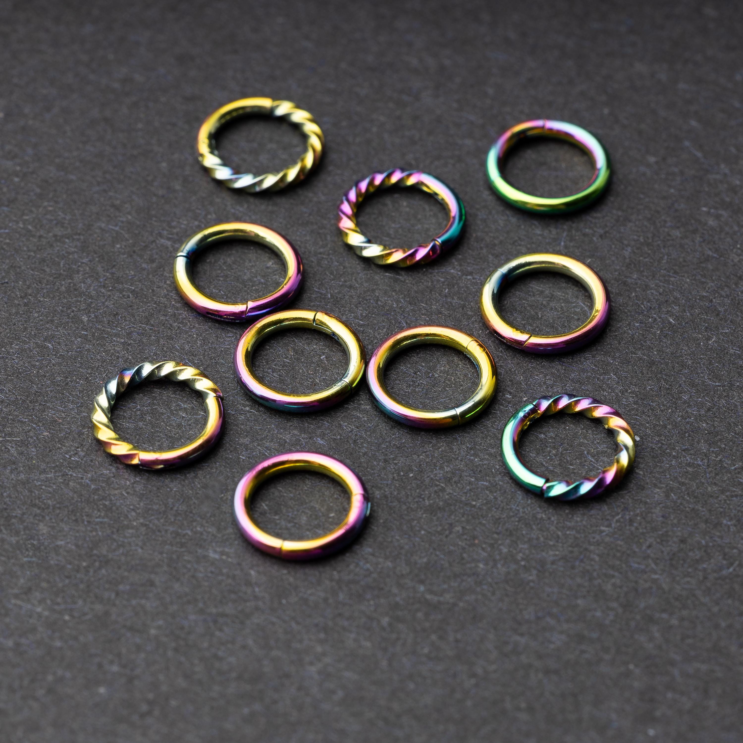Set of rainbow clicker rings with smooth and twisted designs, displayed on a dark background.