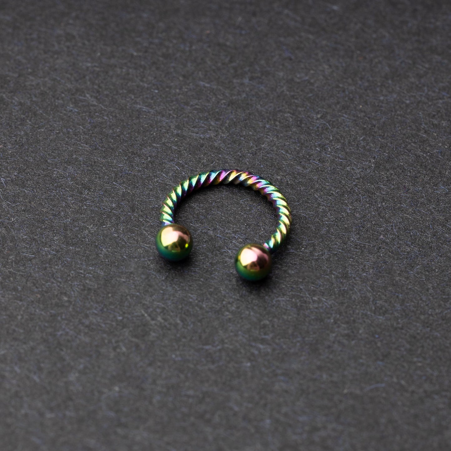 Twisted horseshoe barbells in rainbow finish displayed on a dark background, highlighting their bold and unique design.