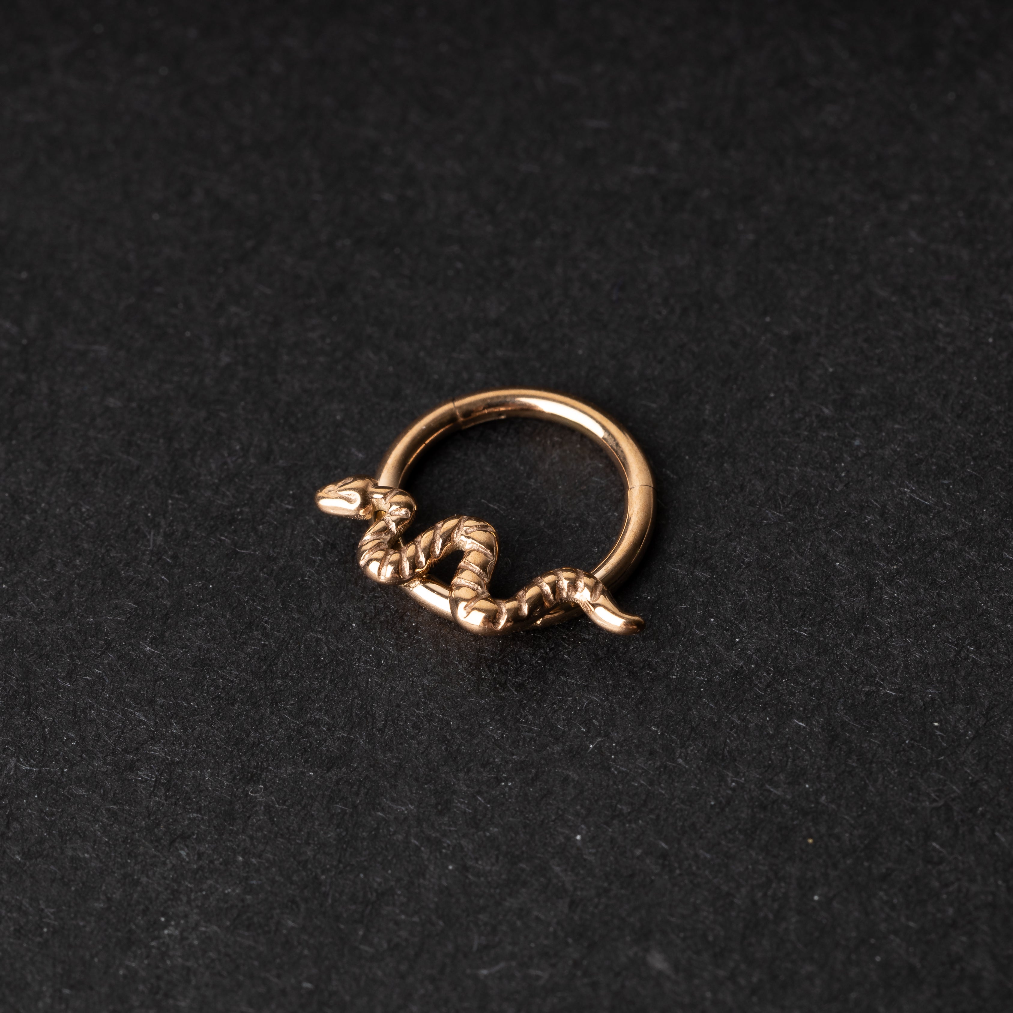 Rose gold snake clicker ring displayed on a dark background