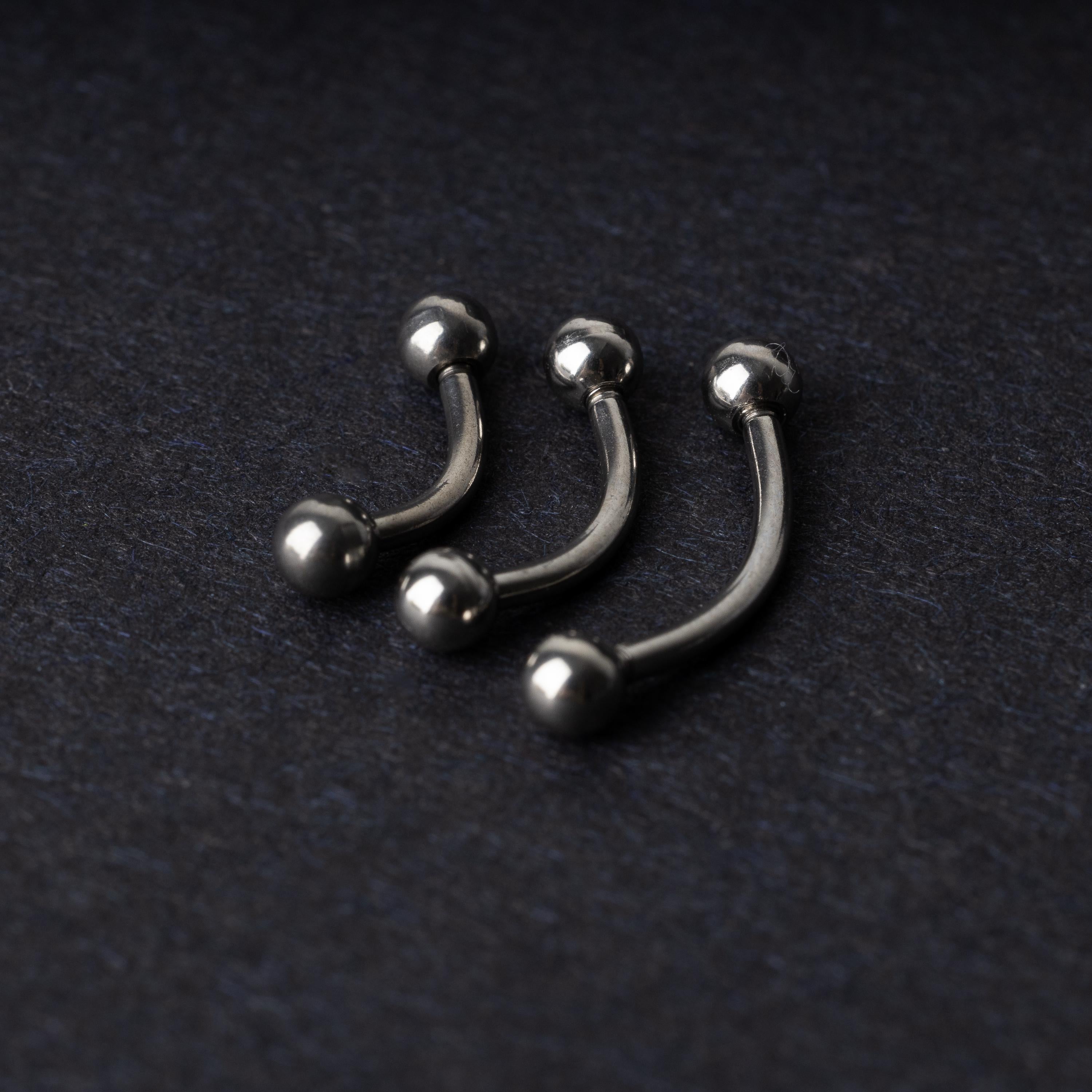 Three silver stainless steel curved barbells with polished ball ends, displayed on a dark textured background.