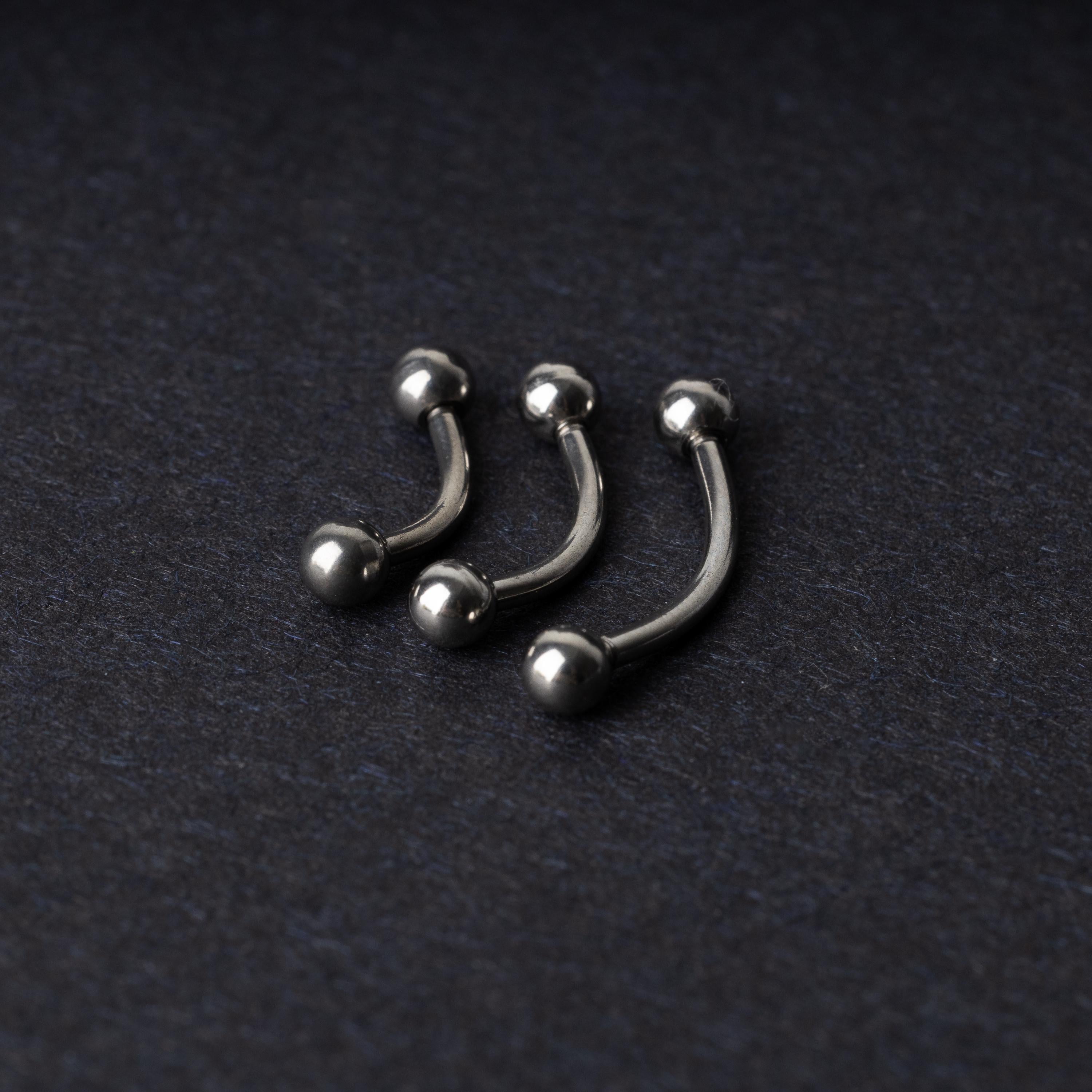 Three silver stainless steel curved barbells with polished ball ends, displayed on a dark textured background.