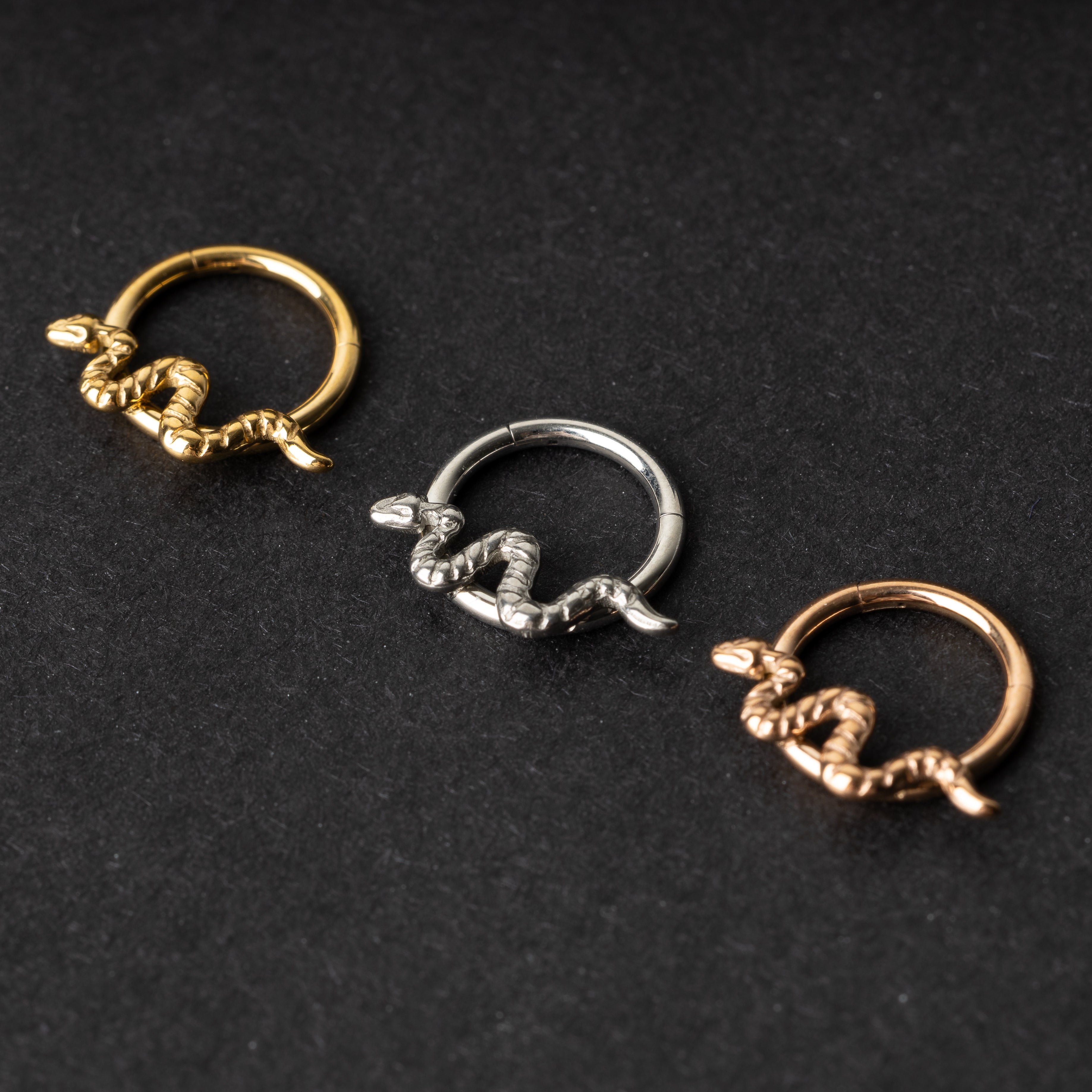 Gold, silver, and rose gold snake motif hinged rings displayed on a dark background.