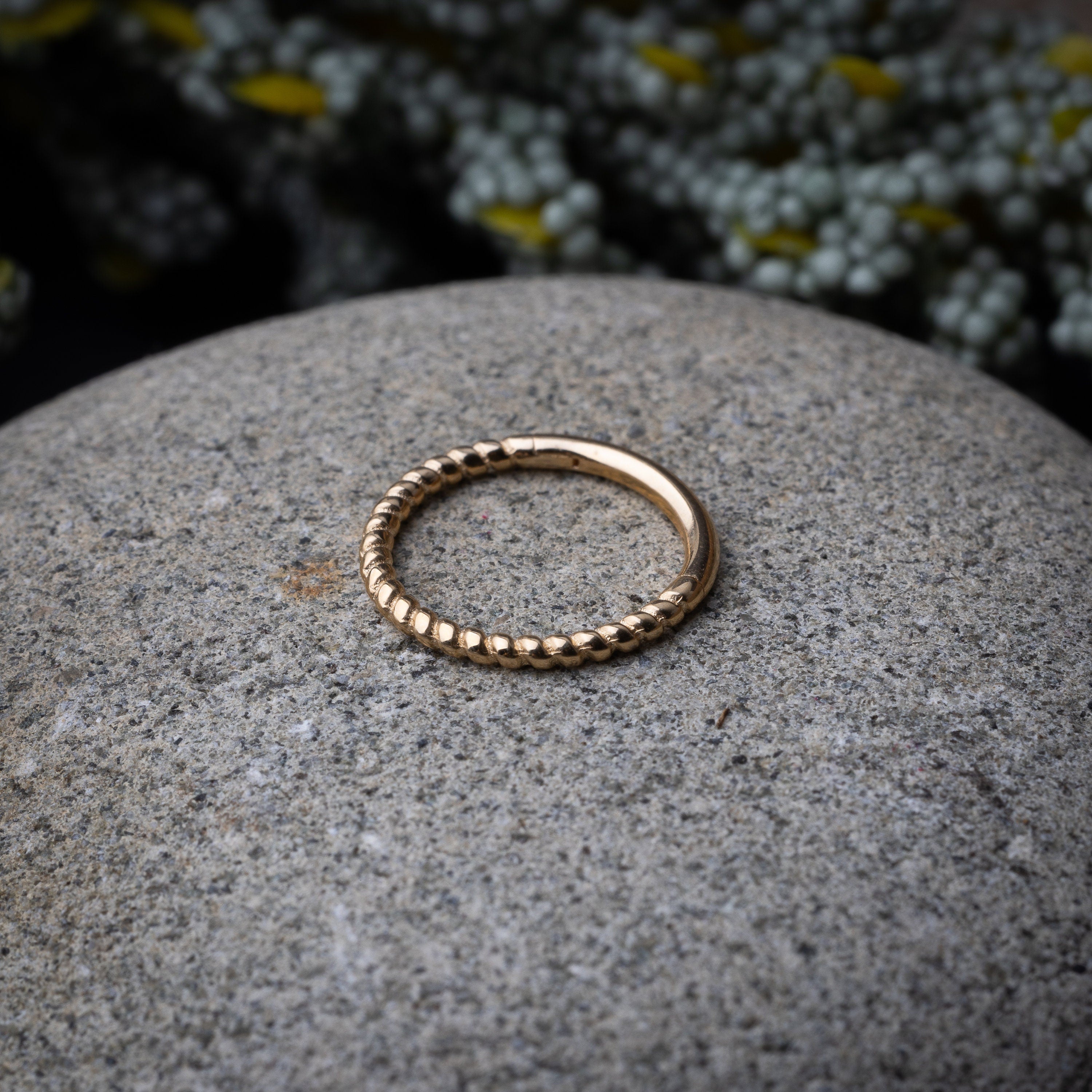 Close-up of a gold rope-textured septum clicker on a stone background, showcasing its intricate design and open hinge mechanism.