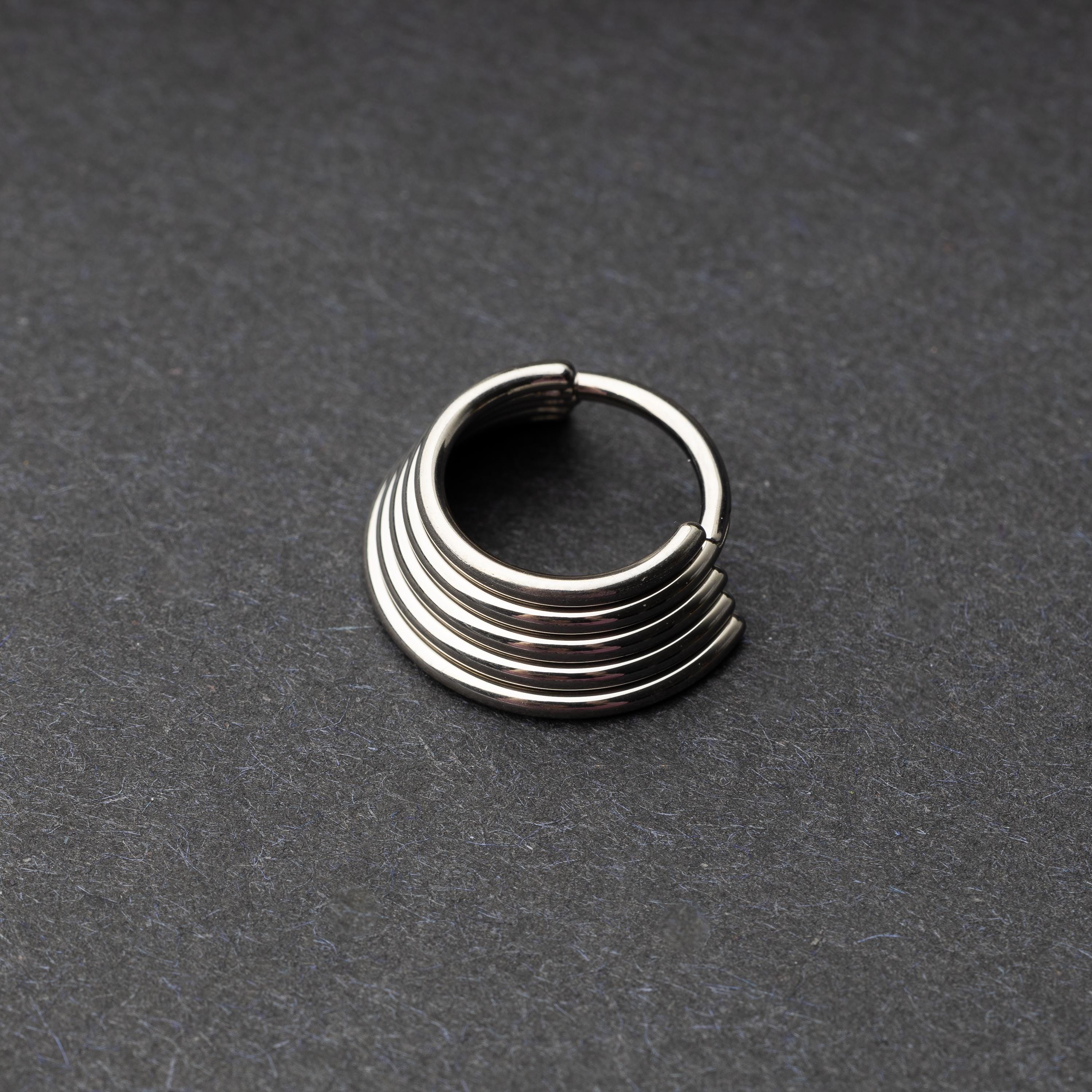 A silver-tone septum clicker with a stacked multi-ring design, displayed on a dark background, showcasing its bold and modern style.