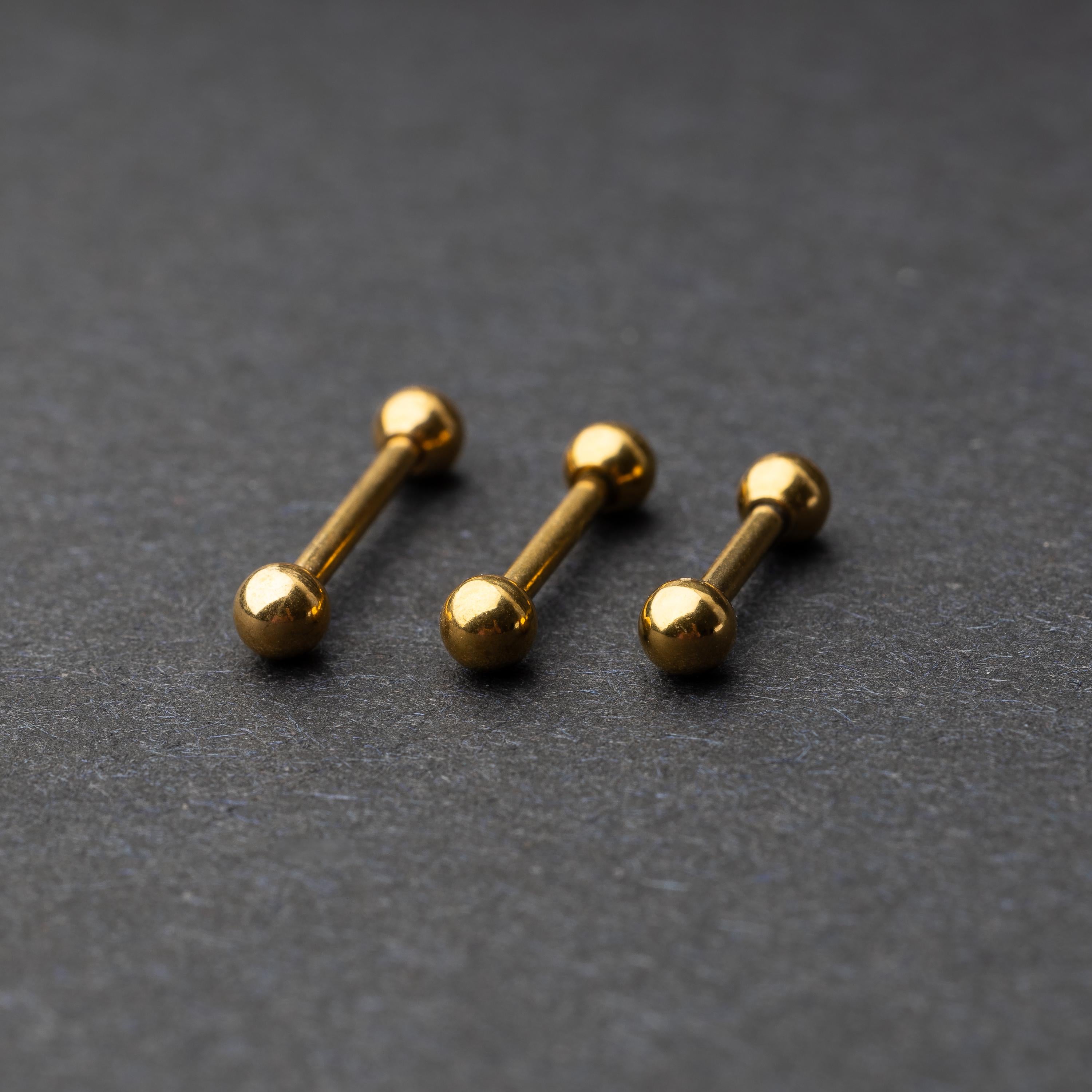 Gold-tone stainless steel barbells with polished spheres on a dark background.