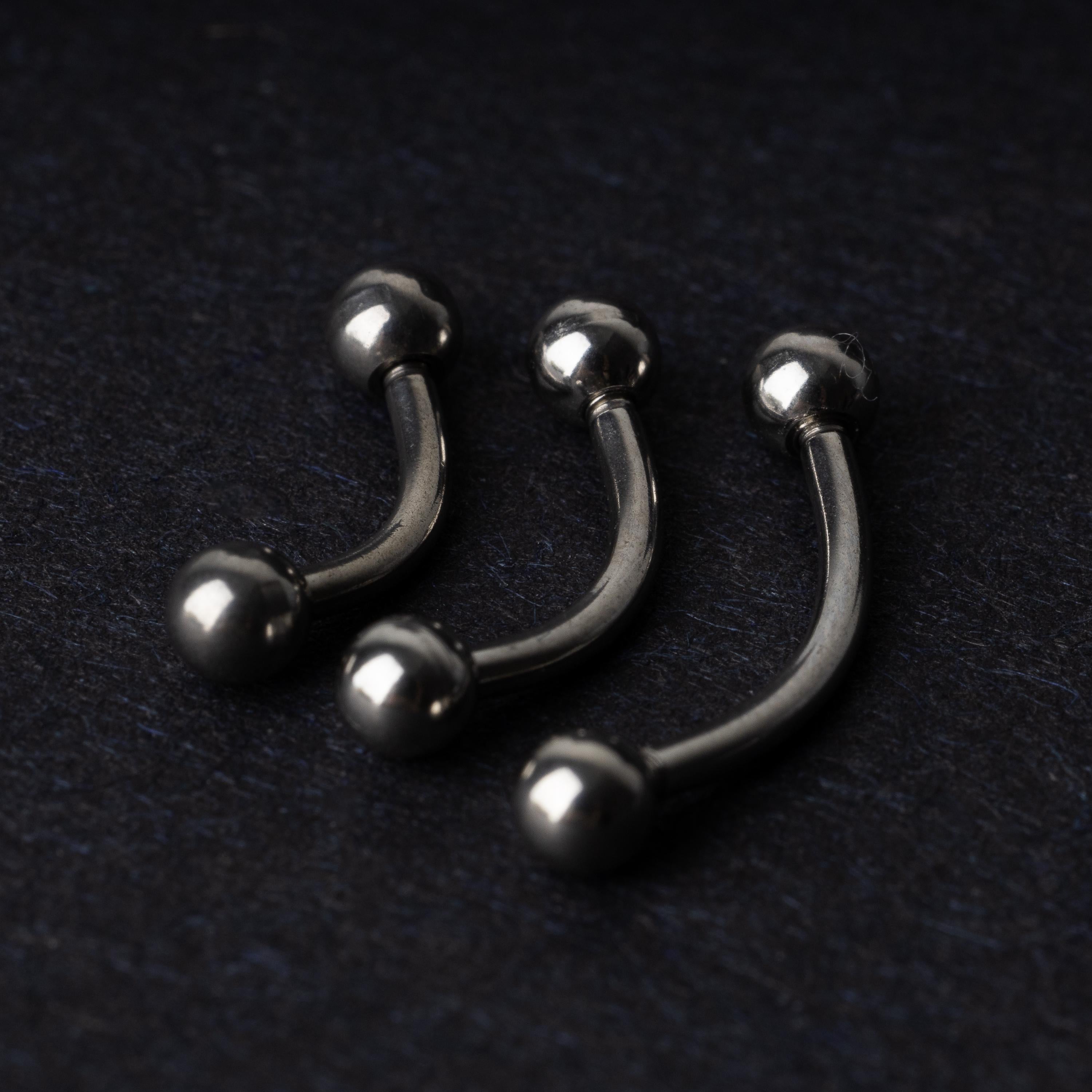 Three silver stainless steel curved barbells with polished ball ends, displayed on a dark textured background.