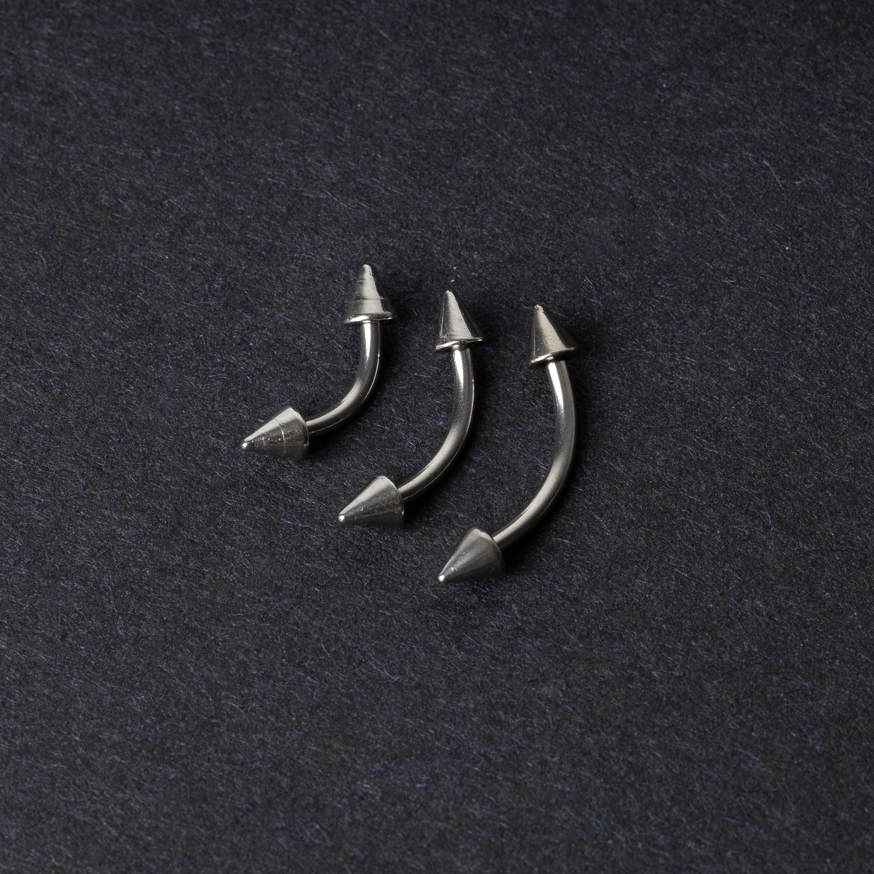 Three stainless steel curved barbells with cone-shaped ends, displayed on a dark background.