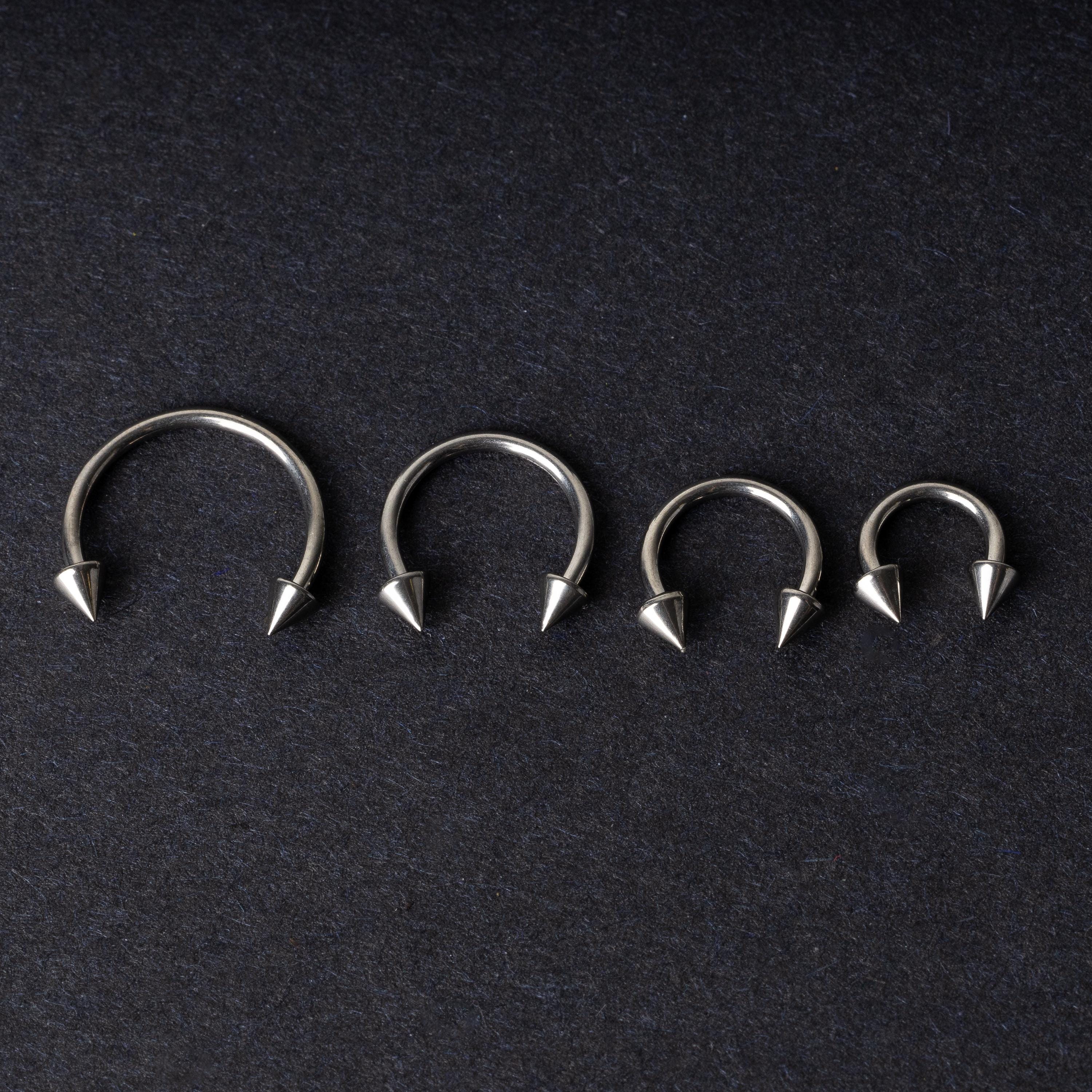 Four titanium horseshoe hoops with pointed cone ends, lined up on a dark background.
