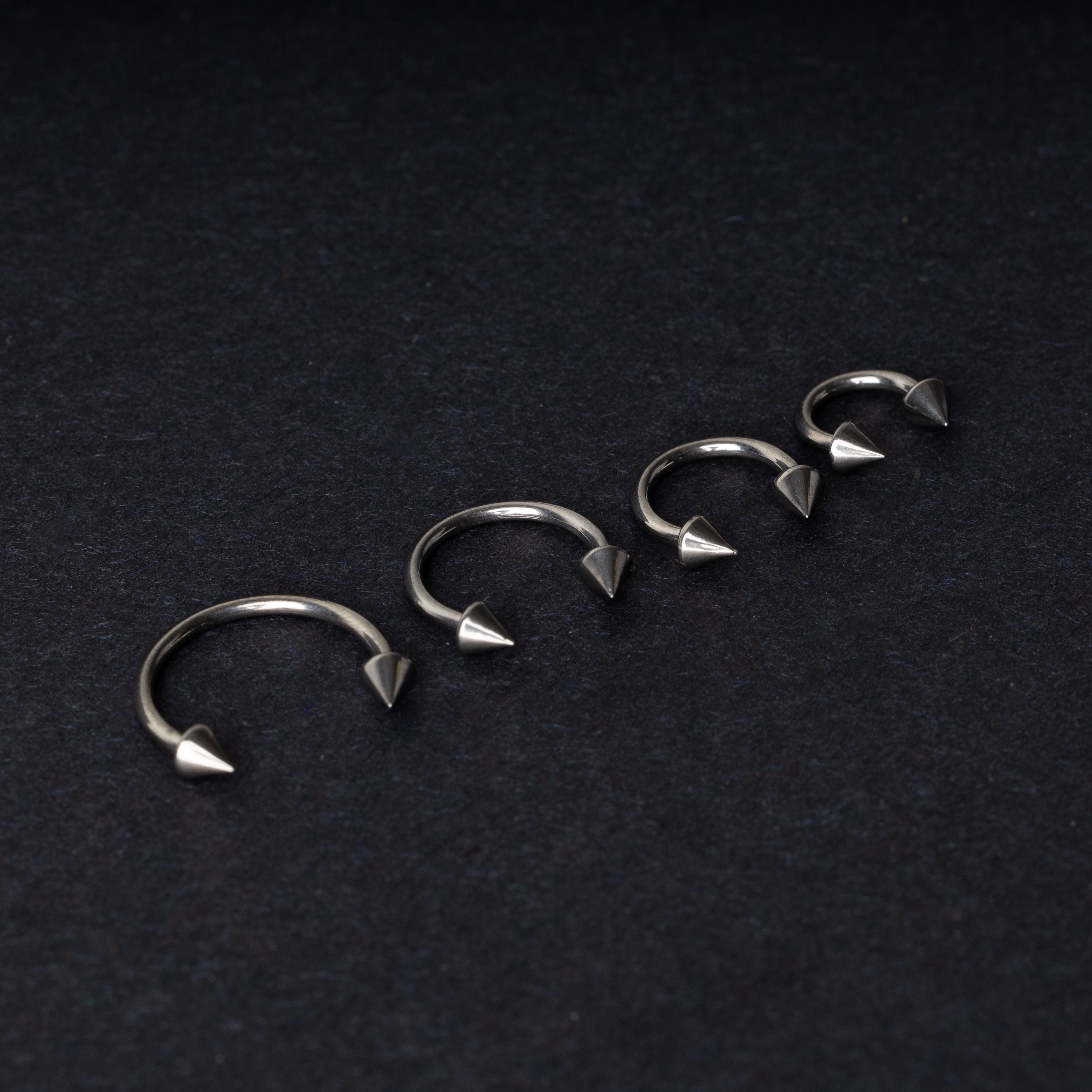Four titanium horseshoe hoops with pointed cone ends, lined up on a dark background.