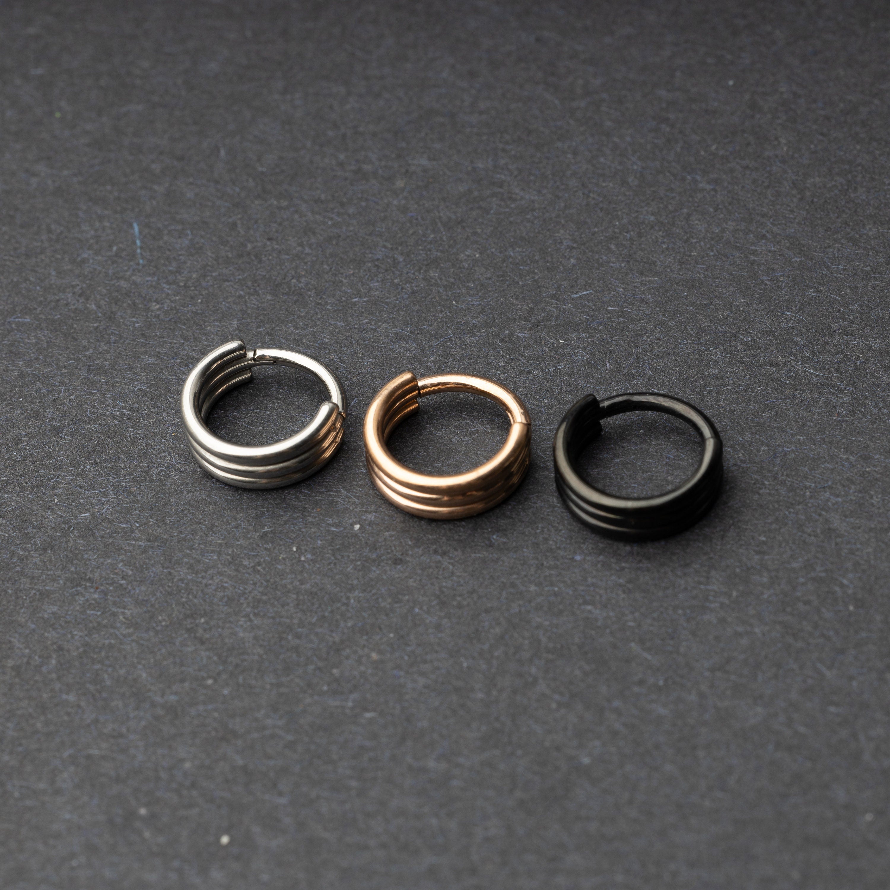 Triple-band seamless hoop rings in silver, gold, and black finishes displayed on a dark background, highlighting their sleek and modern design.