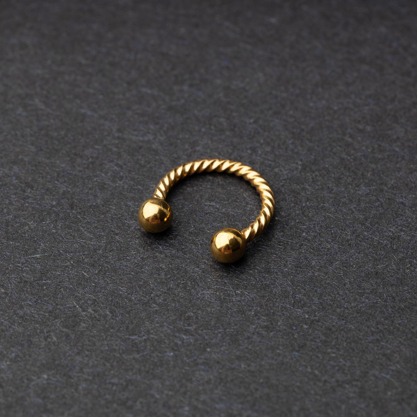 Twisted horseshoe barbells in gold finish displayed on a dark background, highlighting their bold and unique design.