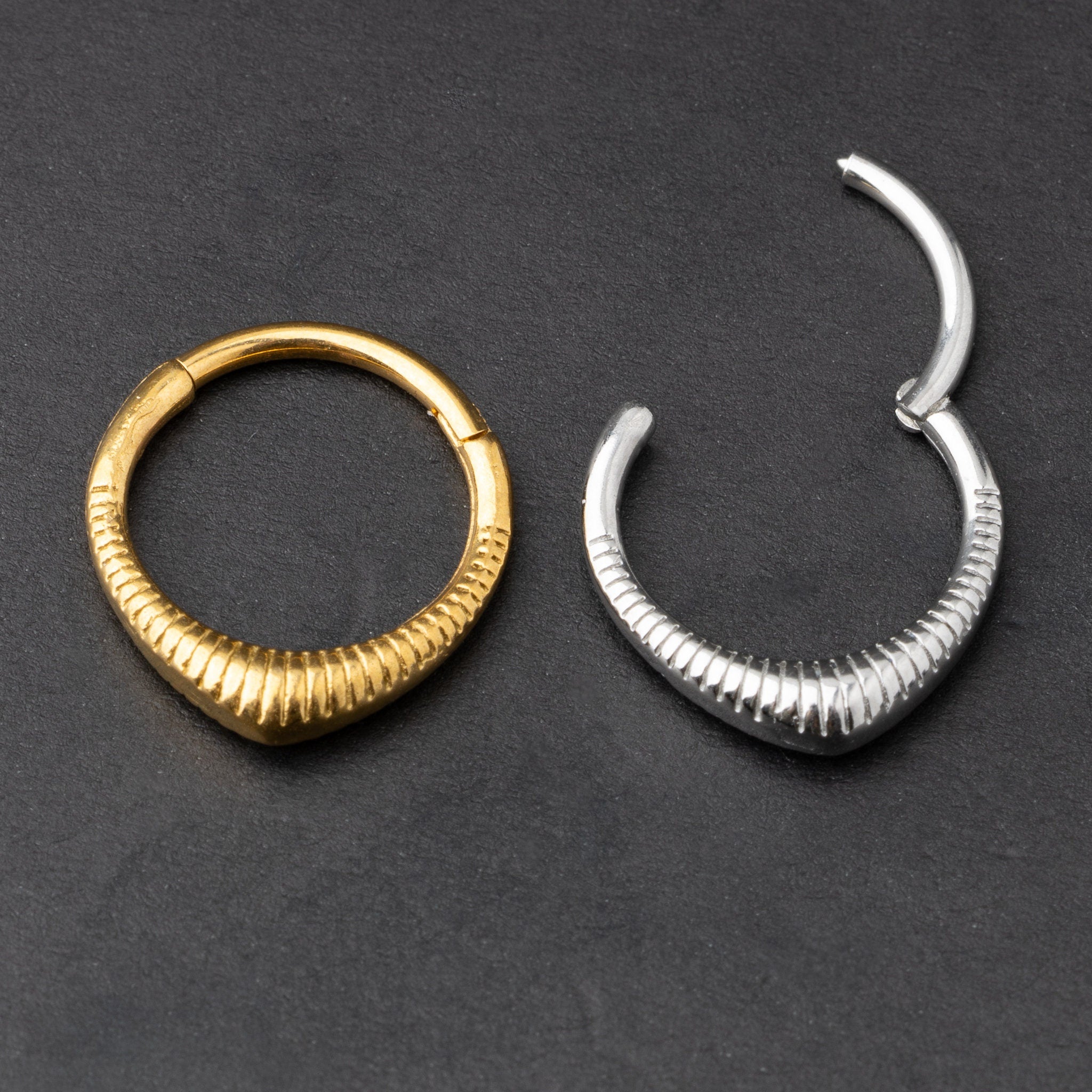 Gold and silver ribbed septum clicker jewelry displayed on a dark background, showcasing a sleek, modern design