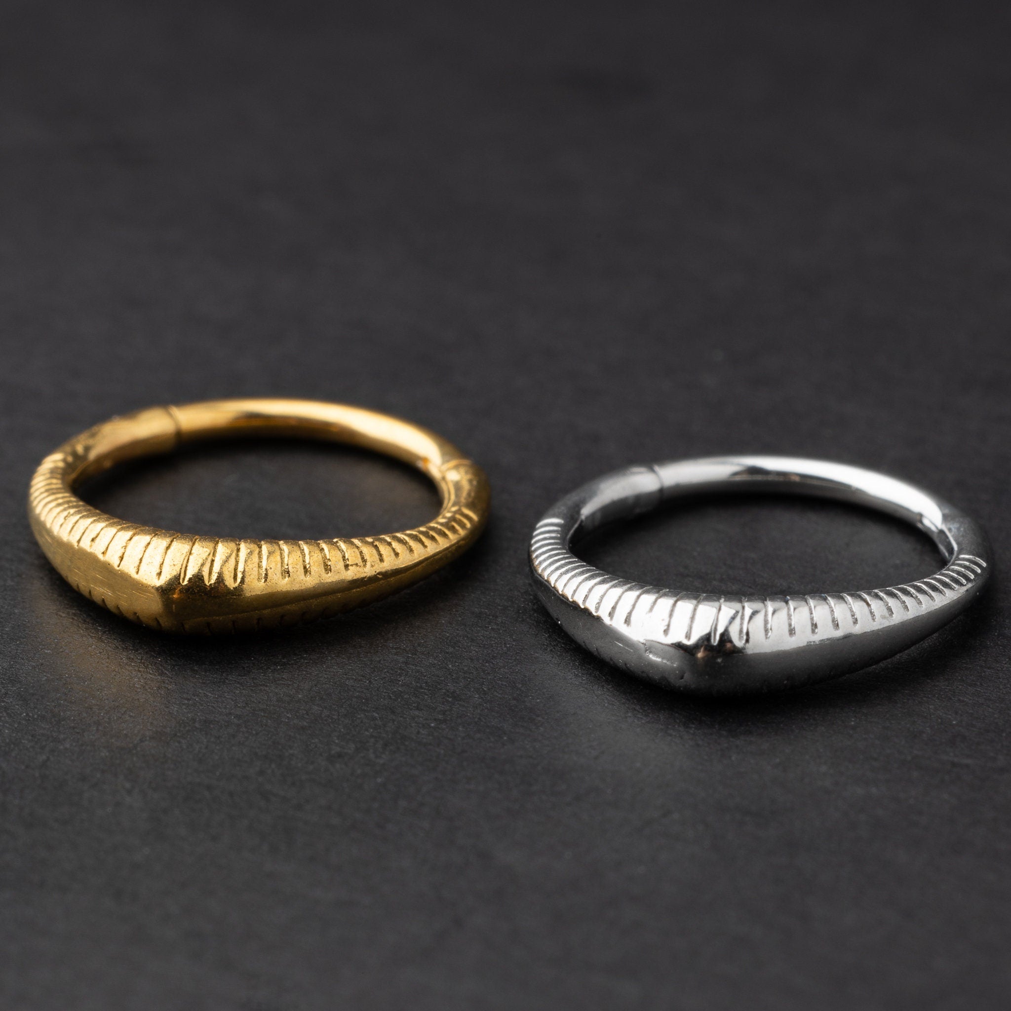 Gold and silver ribbed septum clicker jewelry displayed on a dark background, showcasing a sleek, modern design