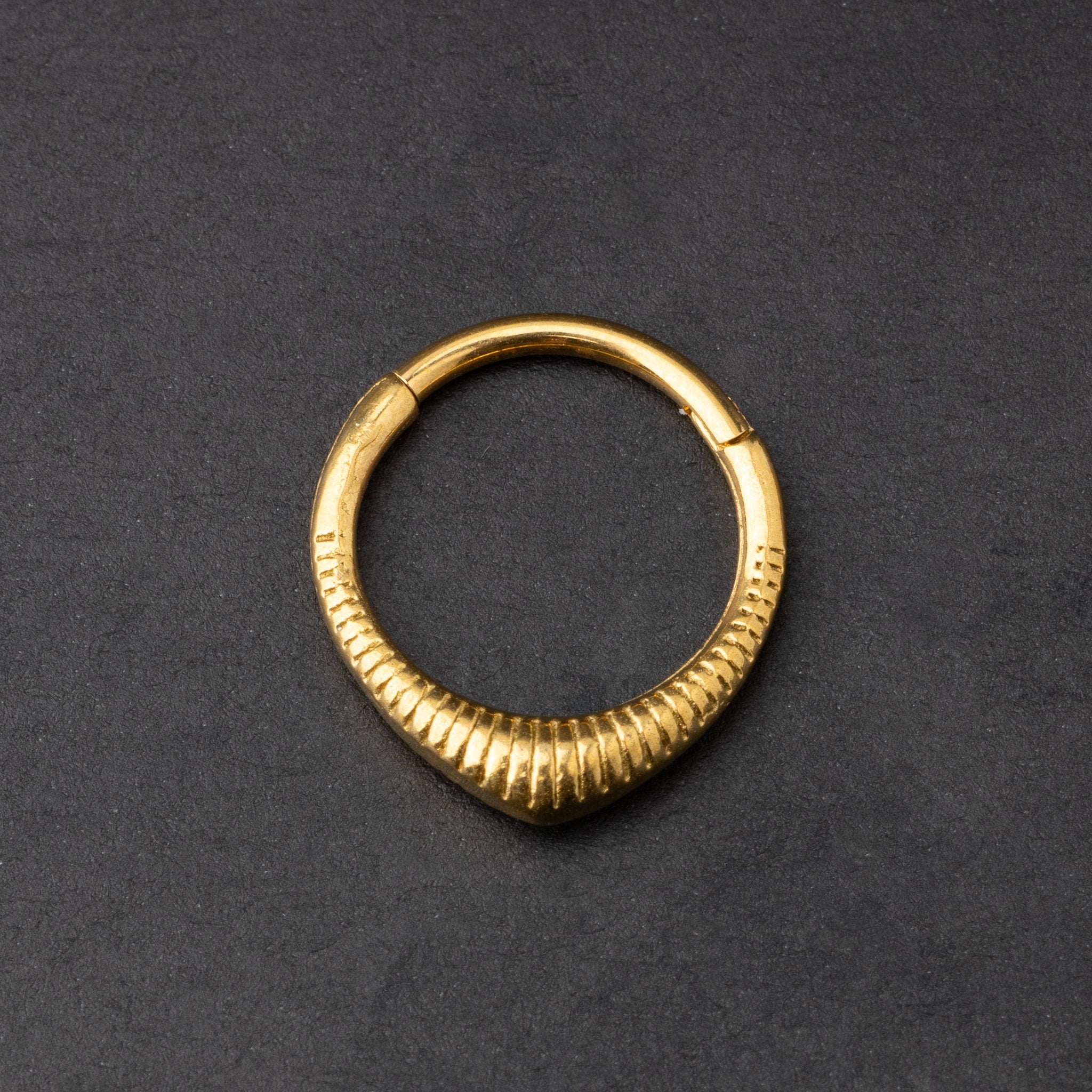 Gold ribbed septum clicker jewelry displayed on a dark background, showcasing a sleek, modern design