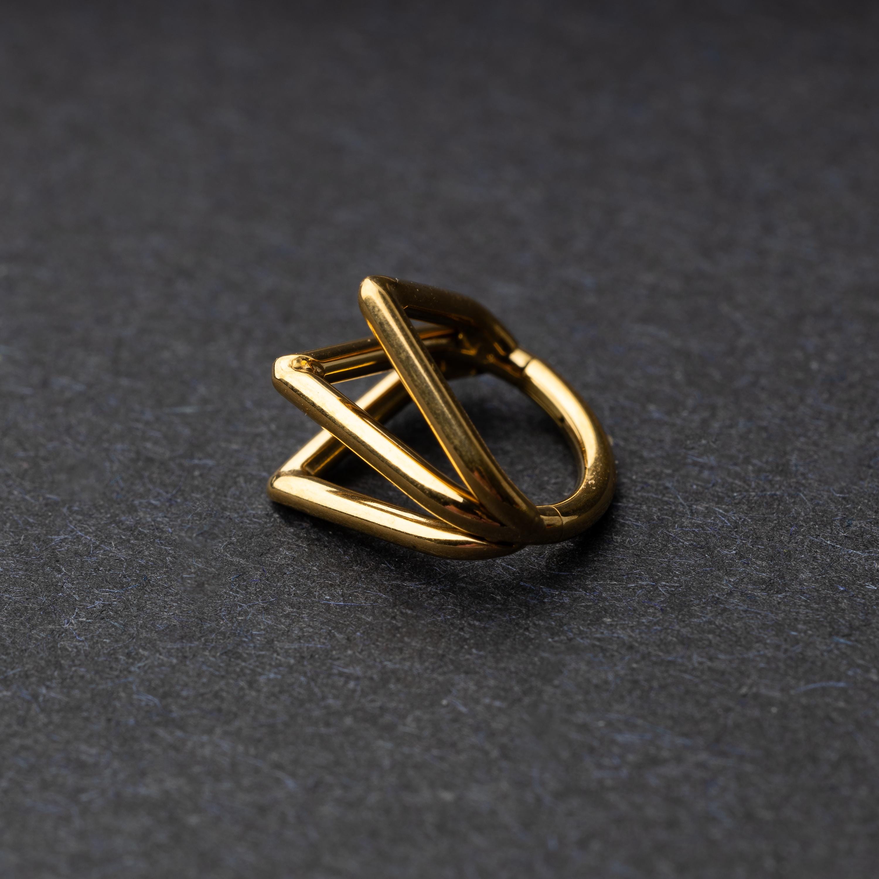 Close-up of a geometric septum clicker in gold, featuring a unique layered triangular design, displayed on a dark background.