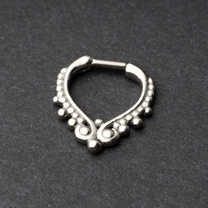 Close-up of a silver septum clicker with a teardrop shape and beaded embellishments, displayed on a dark background with a secure hinged clasp.