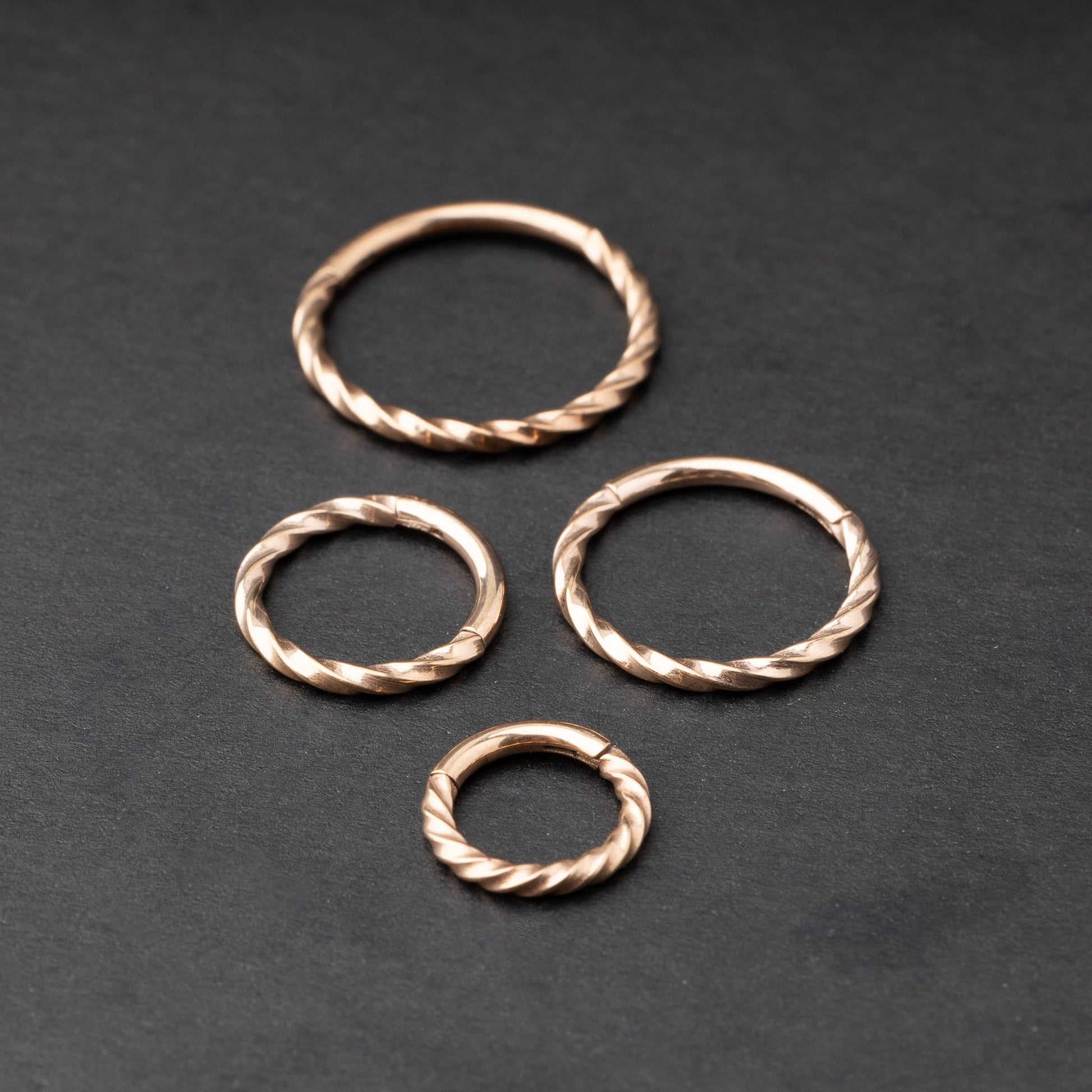 Close-up of a gold hinged ring with a twisted rope design, displayed on a dark background