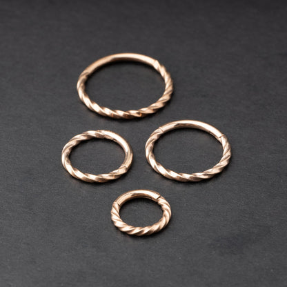 Close-up of a gold hinged ring with a twisted rope design, displayed on a dark background