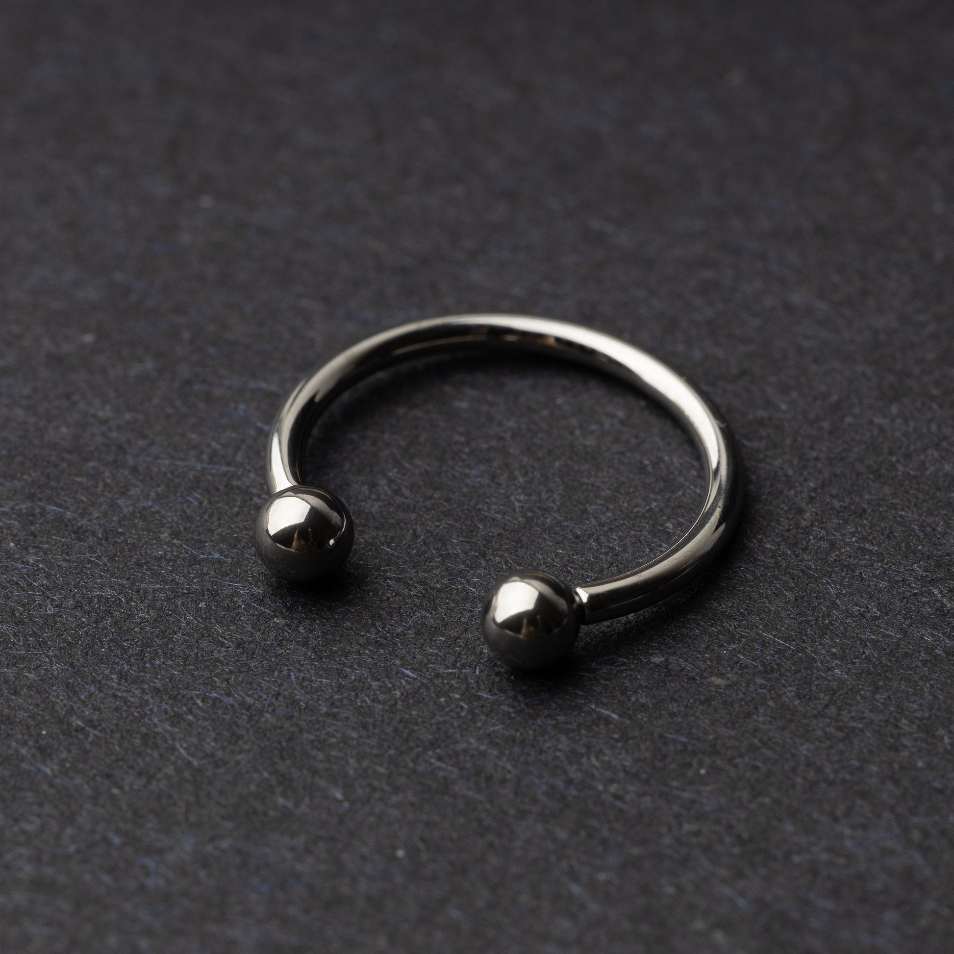 Titanium horseshoe ring with ball ends, displayed on a dark textured background.
