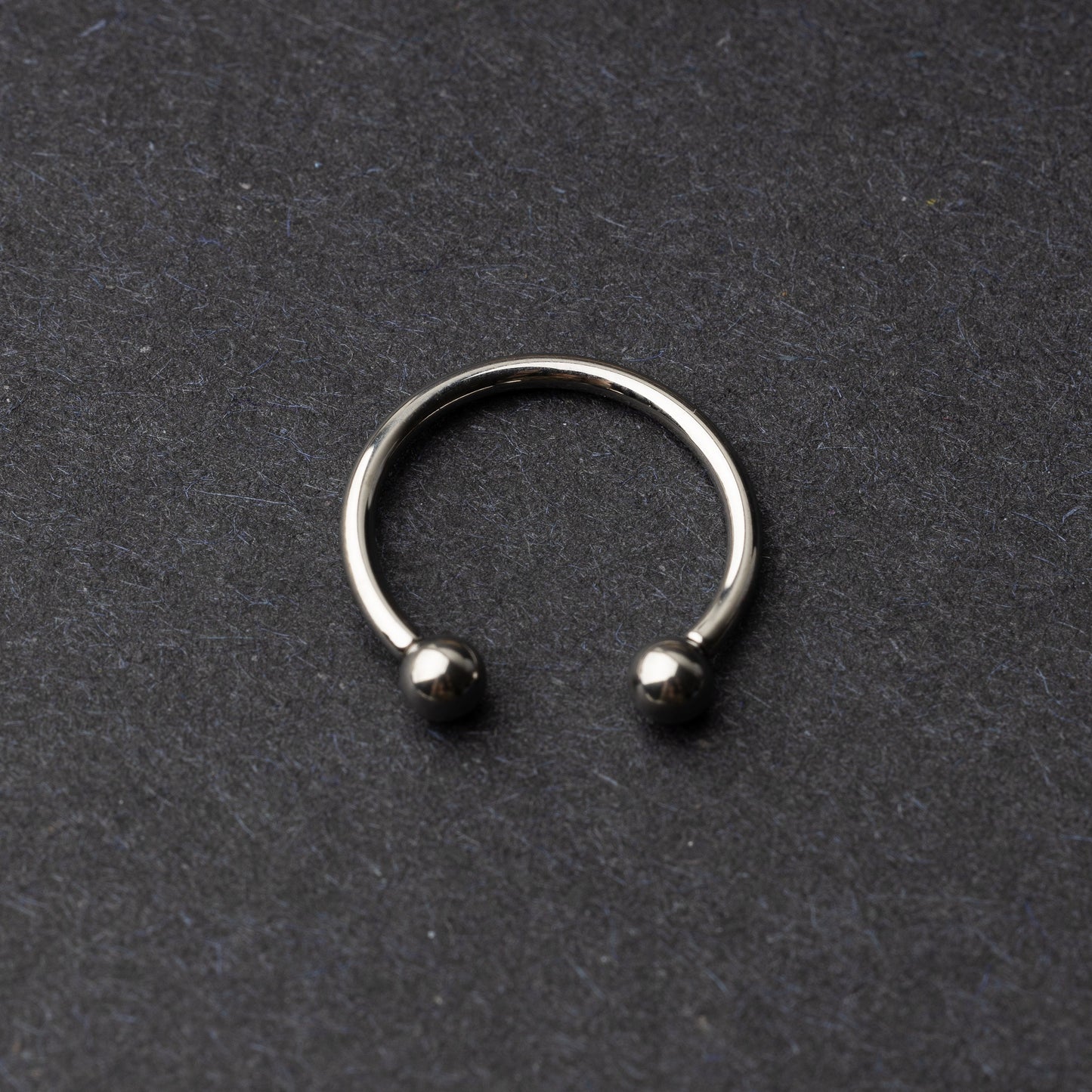Titanium horseshoe ring with ball ends, displayed on a dark textured background.