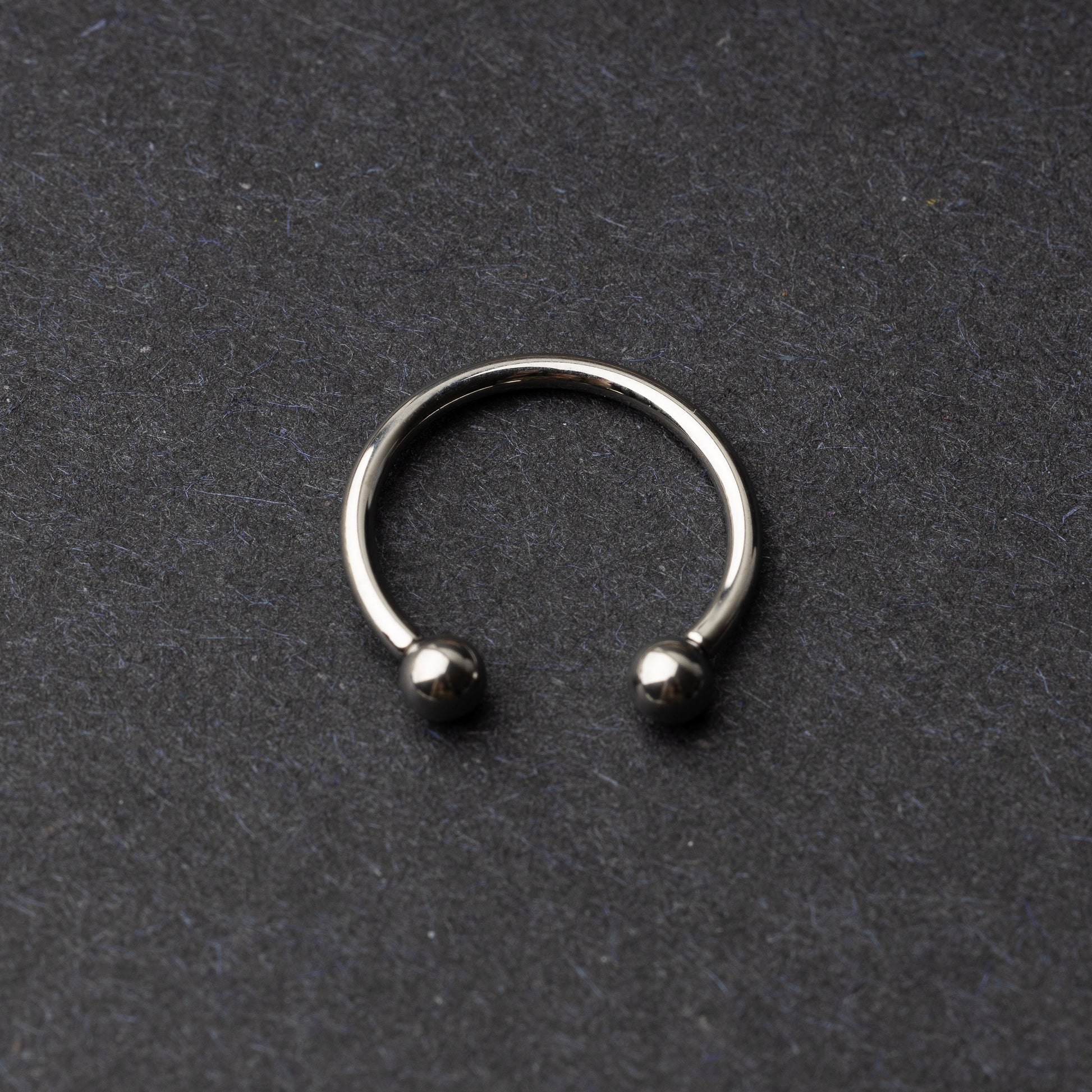 Titanium horseshoe ring with ball ends, displayed on a dark textured background.