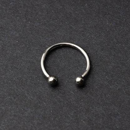 Titanium horseshoe ring with ball ends, displayed on a dark textured background.
