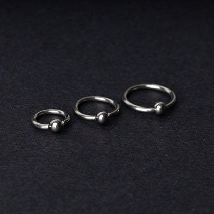 Three polished stainless steel captive bead rings of varying sizes displayed on a dark matte background.