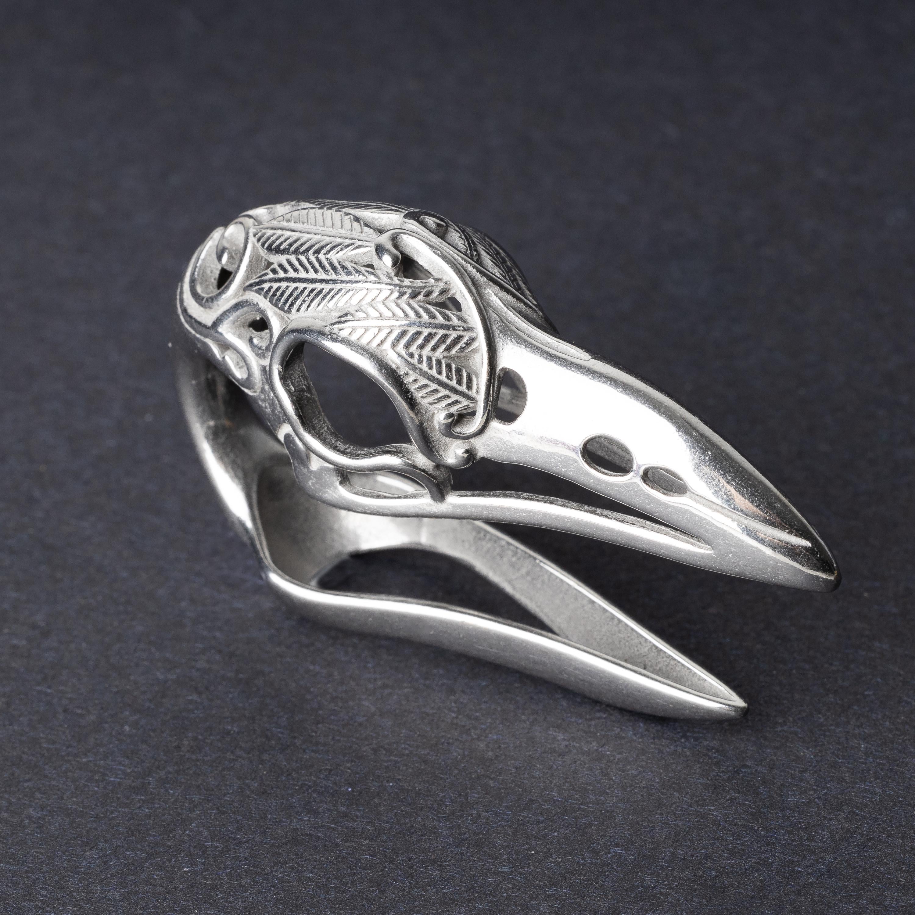 A silver raven skull ear hanger showcasing intricate feather engravings and polished details, displayed on a dark background.