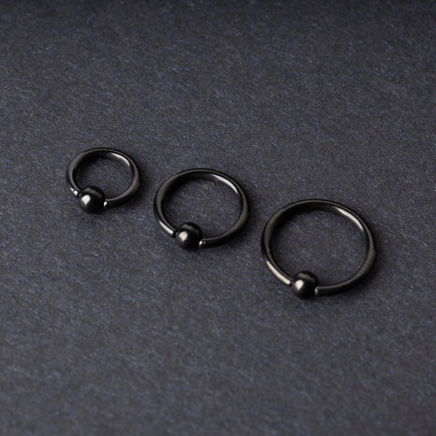 Three black ball closure rings (BCR) in varying sizes, displayed on a dark background with a polished finish and secure captive balls.