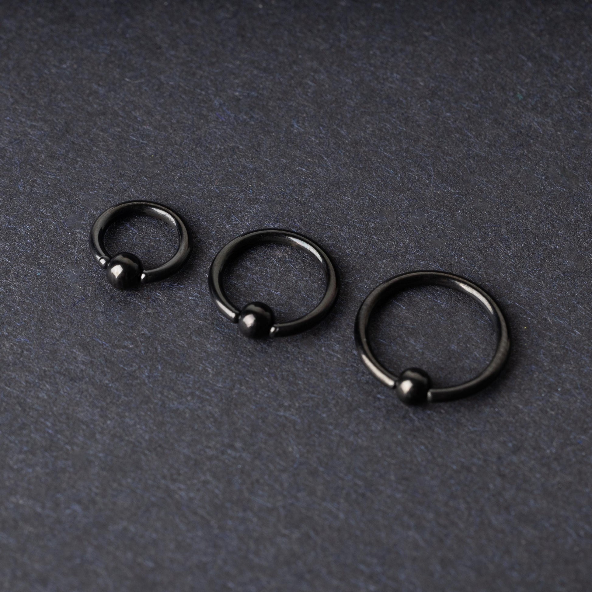 Three black ball closure rings (BCR) in varying sizes, displayed on a dark background with a polished finish and secure captive balls.