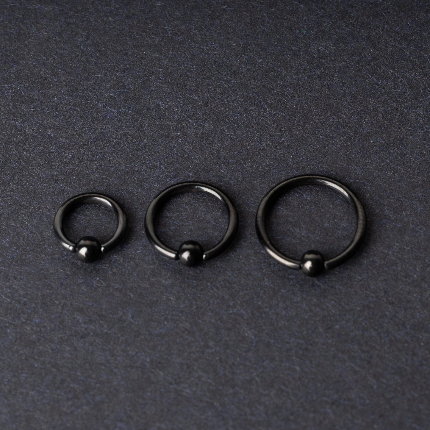 Three black ball closure rings (BCR) in varying sizes, displayed on a dark background with a polished finish and secure captive balls.